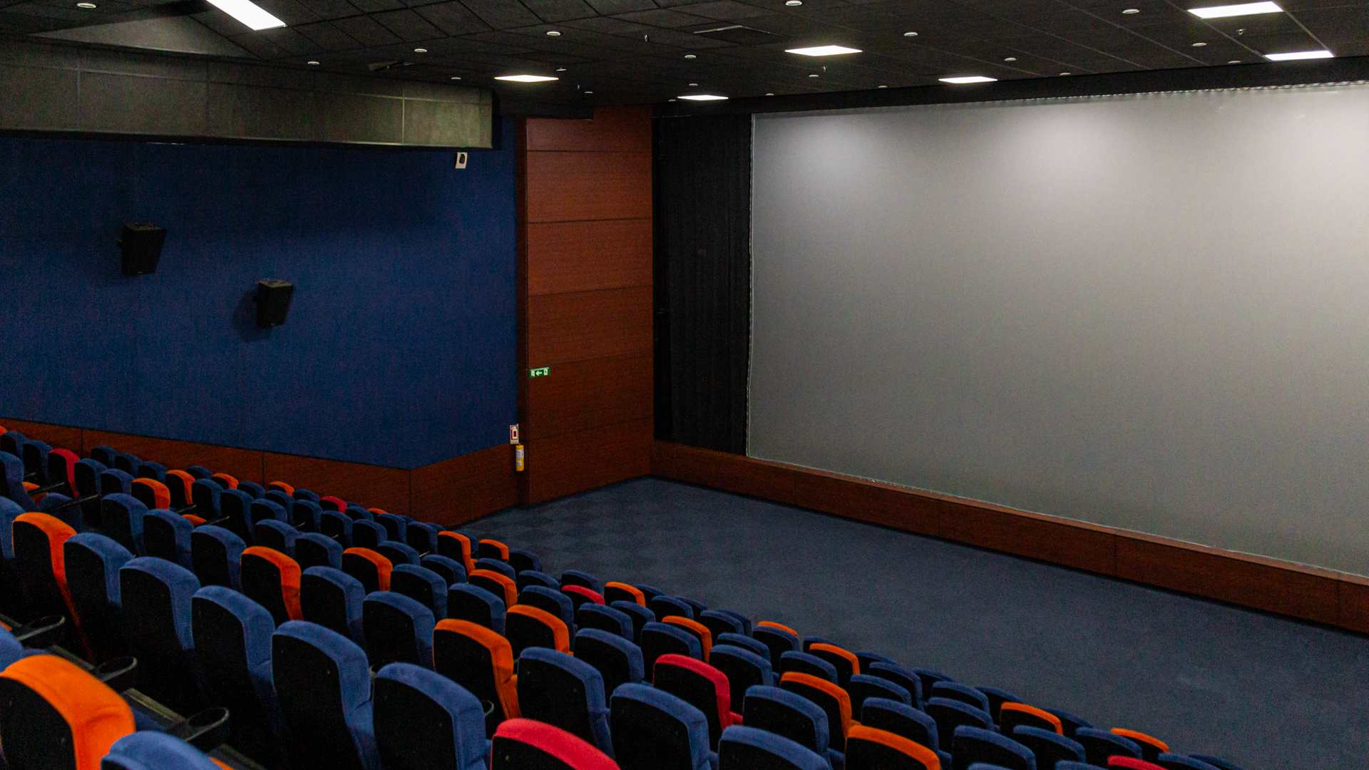 Sala de cine con una pantalla gigante. Al frente hay varias filas de sillas de colores y cómodas.