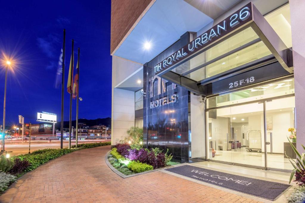  Entrada de un edificio de noche en la que sobresale un aviso con una leyenda que dice: " nH Royal Urban 26". Al lado hay unas banderas en un asta. 