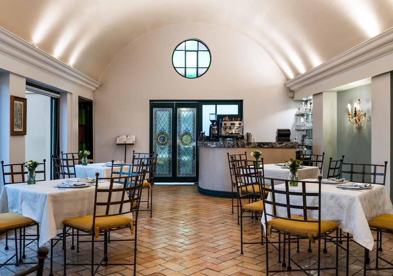  Pequeño salón como comedor en el que hay cuatro mesas con sillas alrededor. Hay un mesón al fondo.
