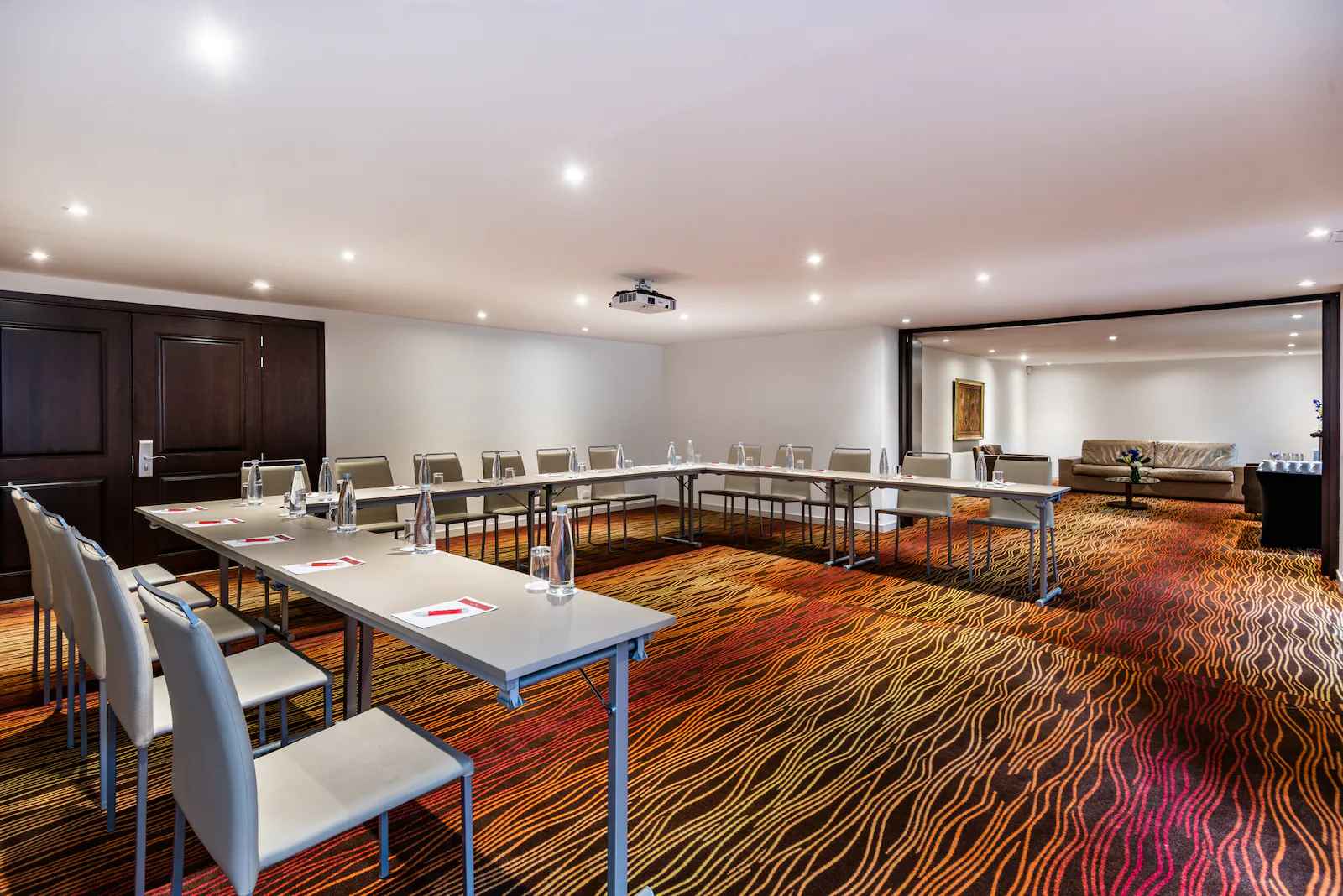 Gran salón en el que se observan unas mesas organizadas en forma de U, y al fondo una sala de estar con un amplio sofá en cuero.