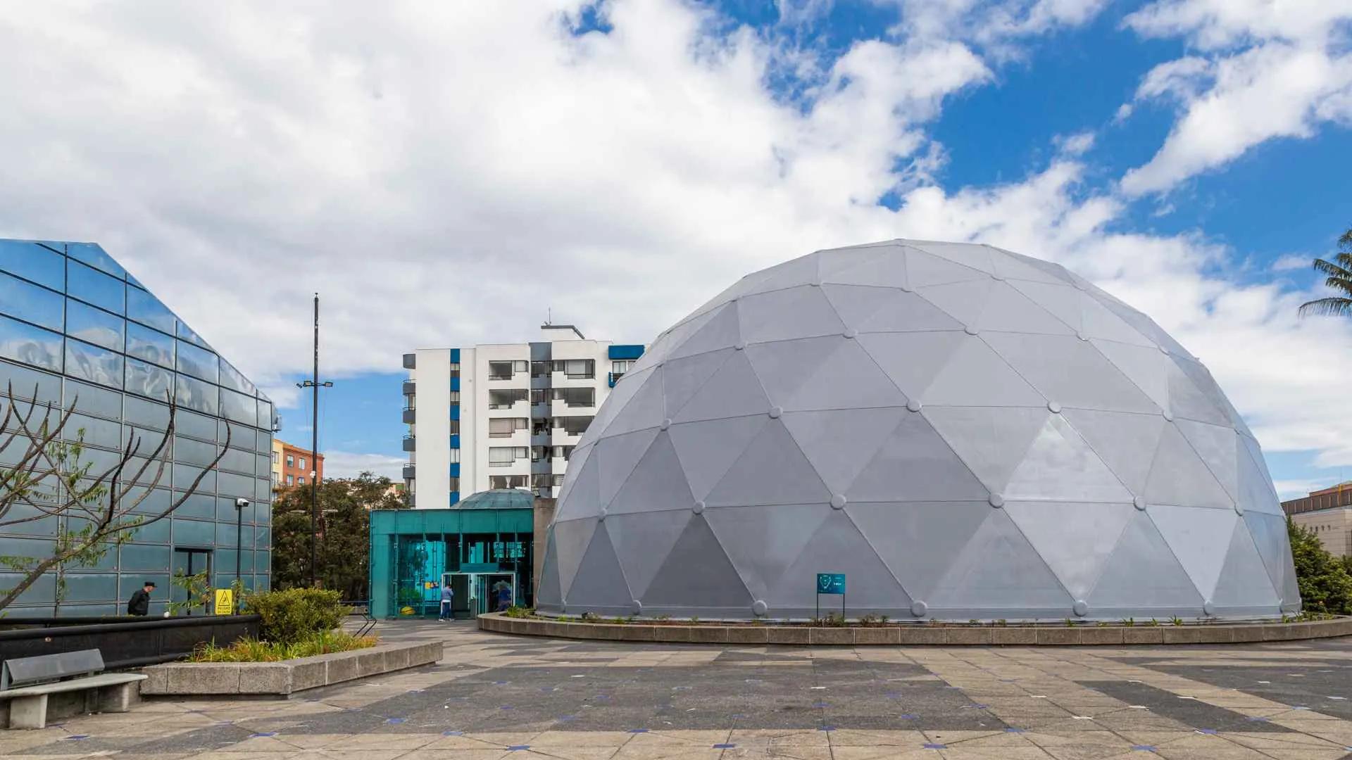 Exterior view of Maloka, a gray metal and concrete dome in a plaza with another gray glass building.