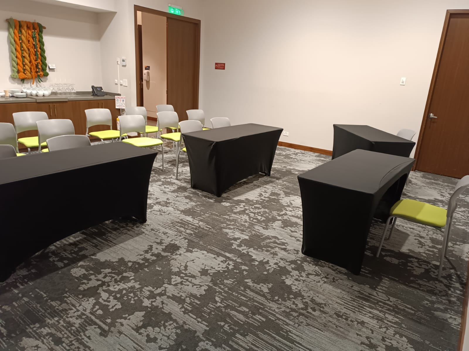 Salón pequeño con cuatro mesas medianas con mantel negro, algunas sillas y una mesa con pocillos.