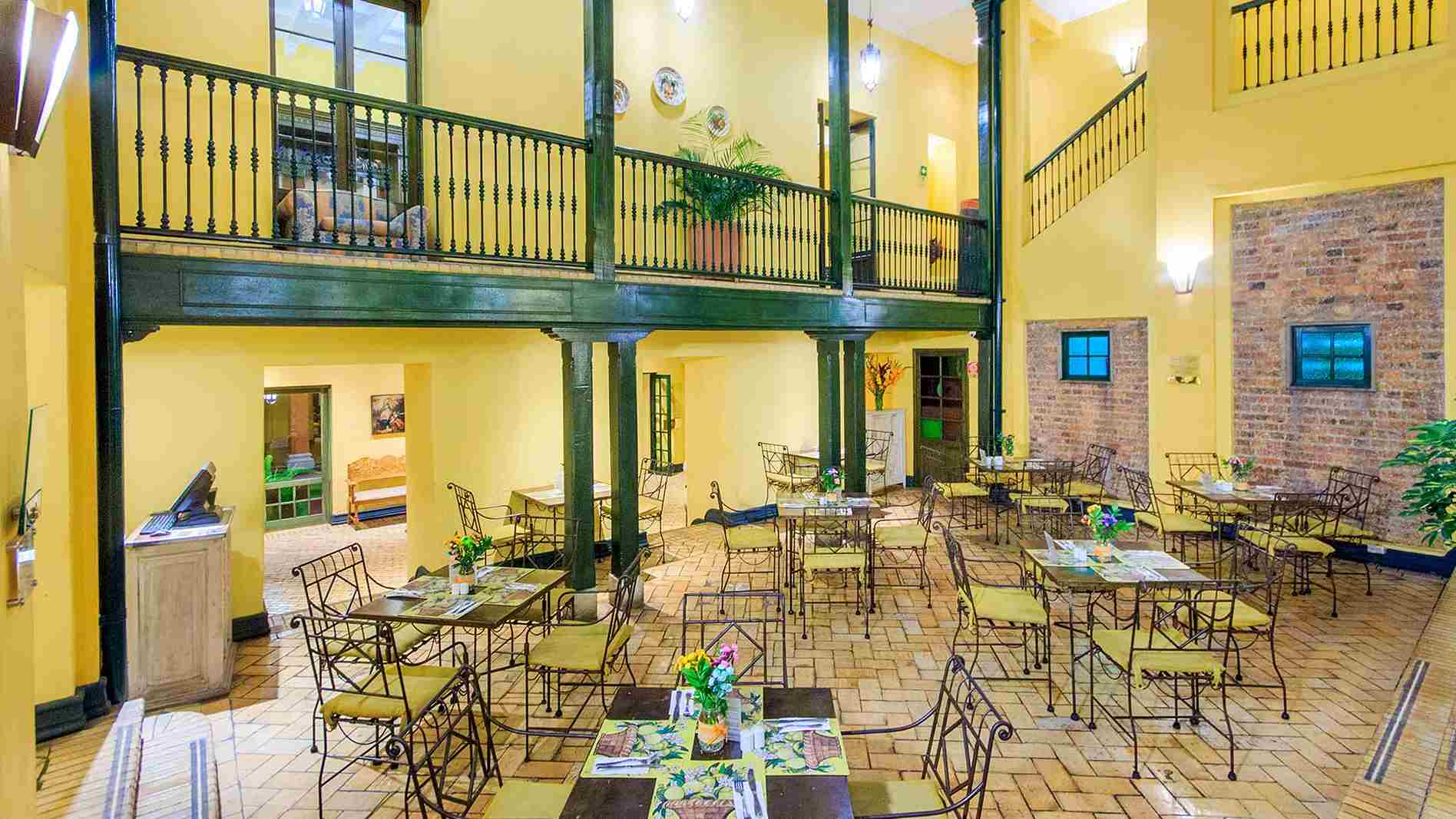 Salón en un primer piso, como un restaurante por las mesas y las sillas que las rodean. Es un edificio de estilo antiguo con un largo balcón de madera y pintado de amarillo.