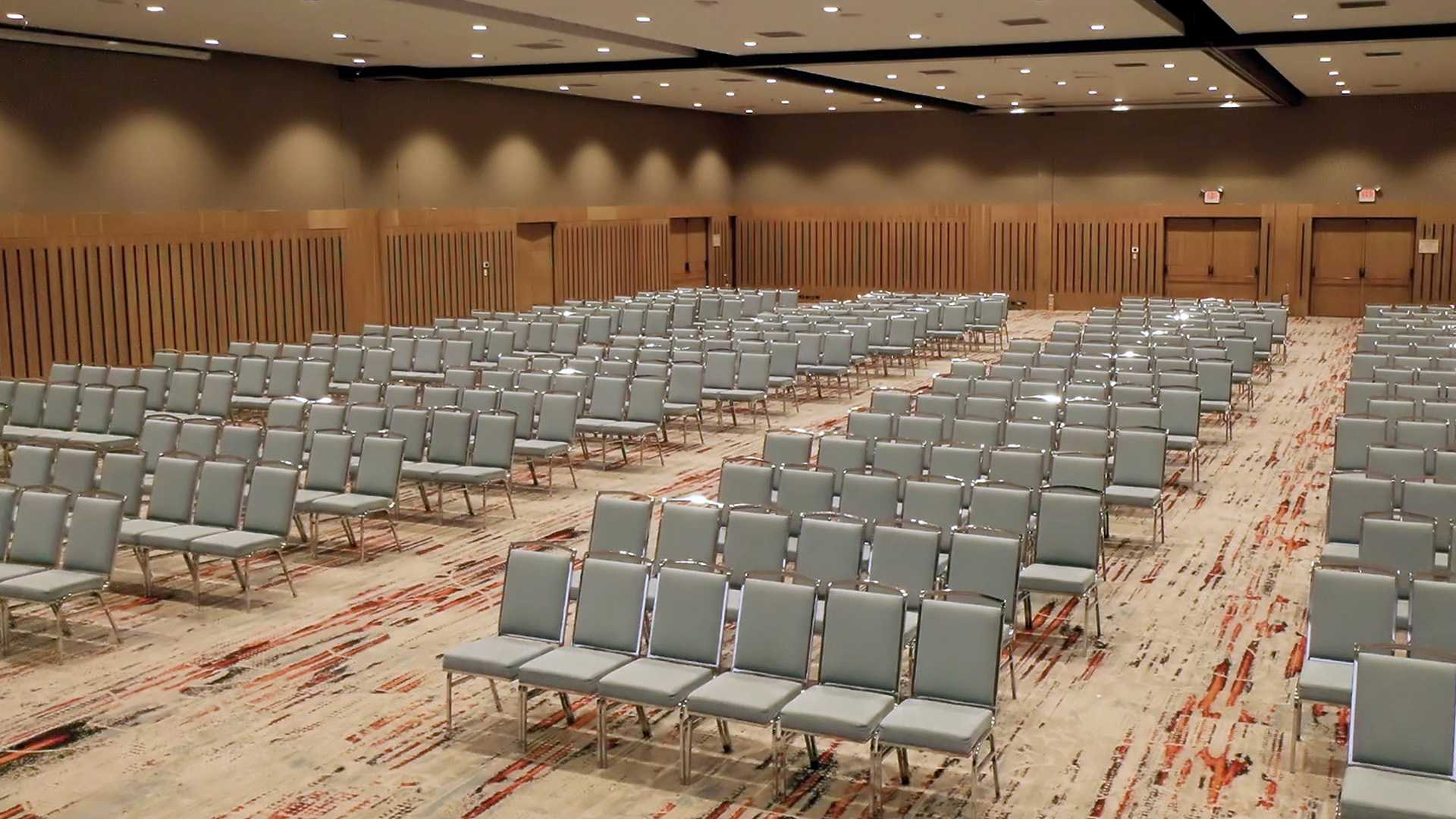 Gran salón decorado con madera con por lo menos un centenar de sillas grises.