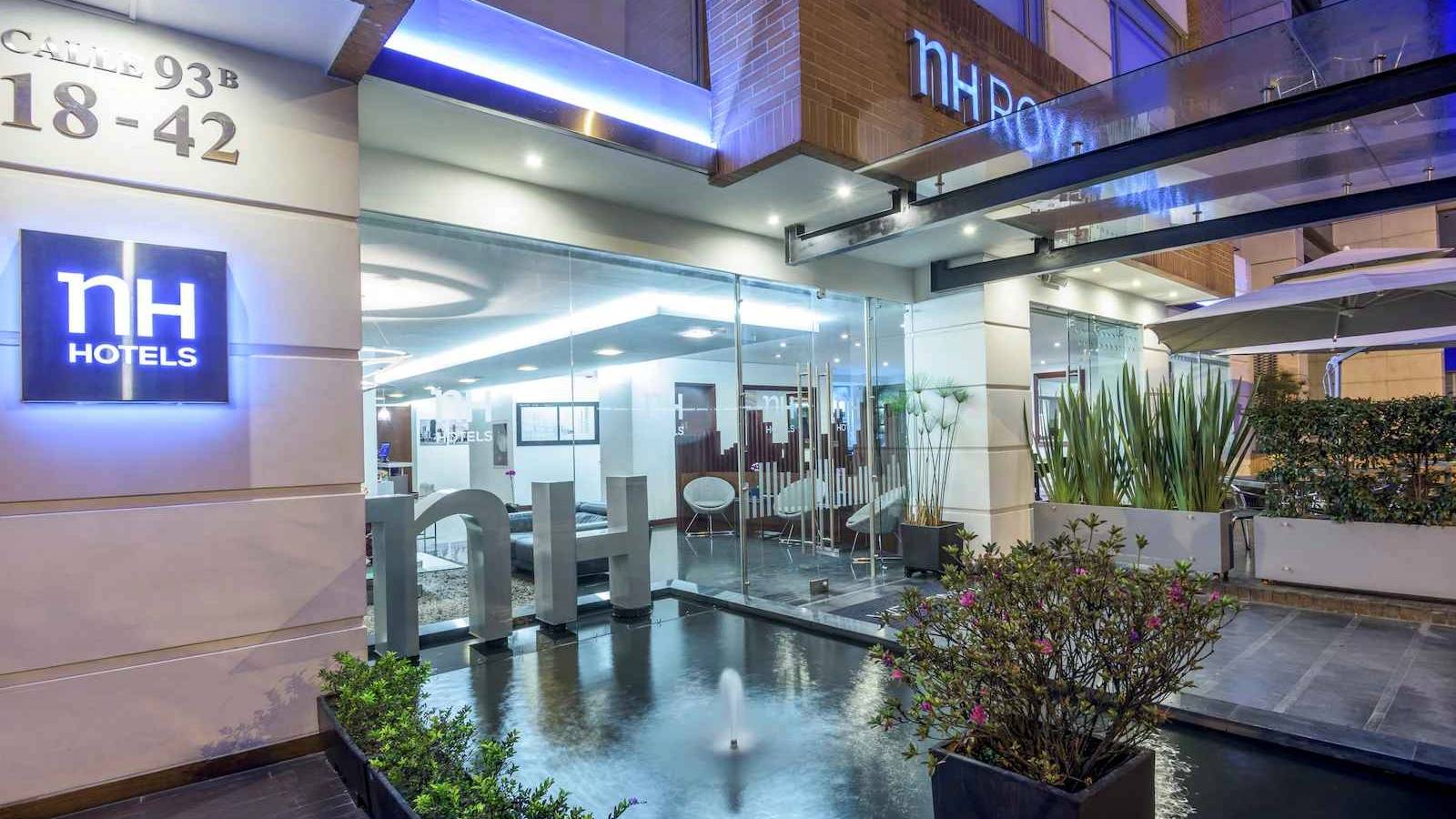 Fachada de entrada principal de un edificio de noche en el que resaltan las paredes en ladrillo, materas y un aviso con una leyenda que dice: "nH Royal Urban 93"