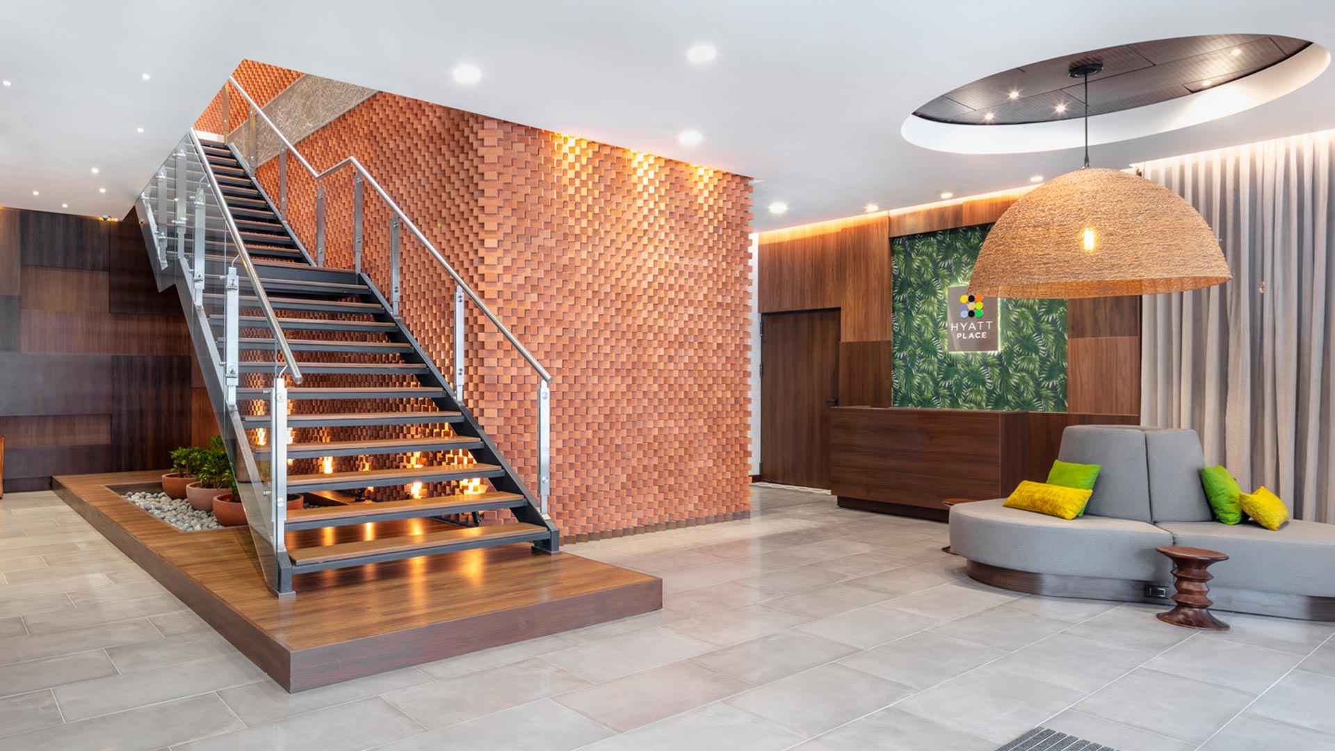 Salón como un lobby donde hay una escalera al lado de una pared de ladrillo, un sofá y un recibidor. Una gran lámpara cuelga del techo. 