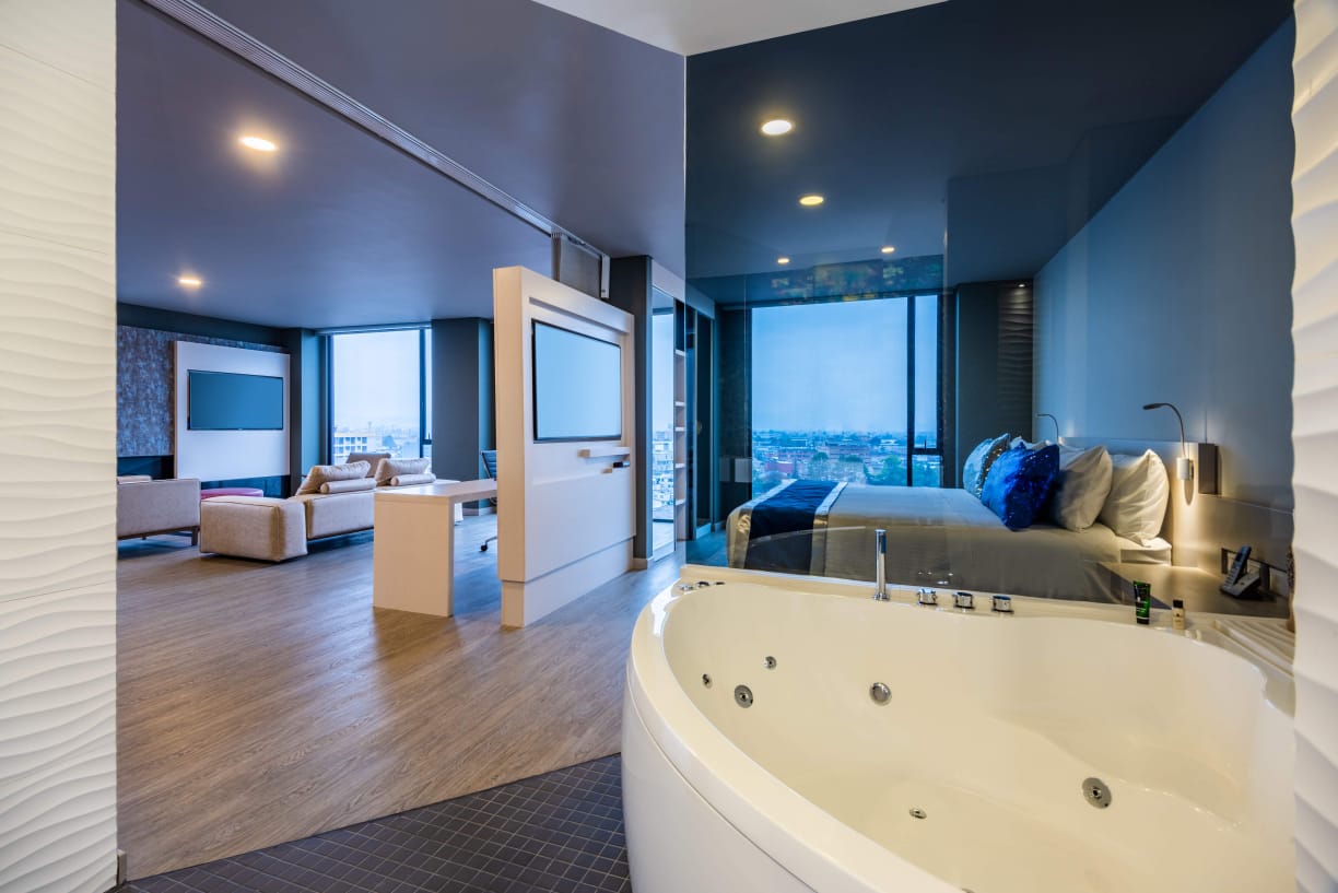 En dos espejos se refleja lo que es una habitación con un jacuzzi, una cama grande y una sala de estar con dos sofás.