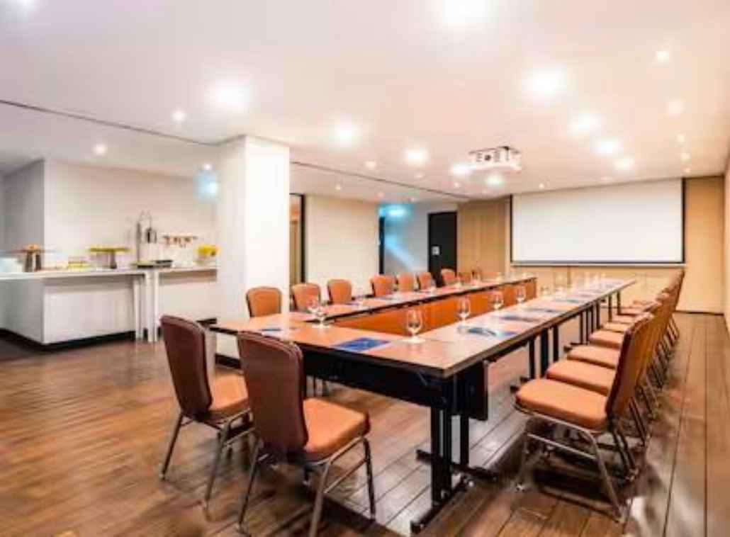 Salón con mesas organizadas en forma de U. Hay varias sillas rodeando la mesa y en ella varias copas de cristal. Al frente hay una pantalla de videobeam.