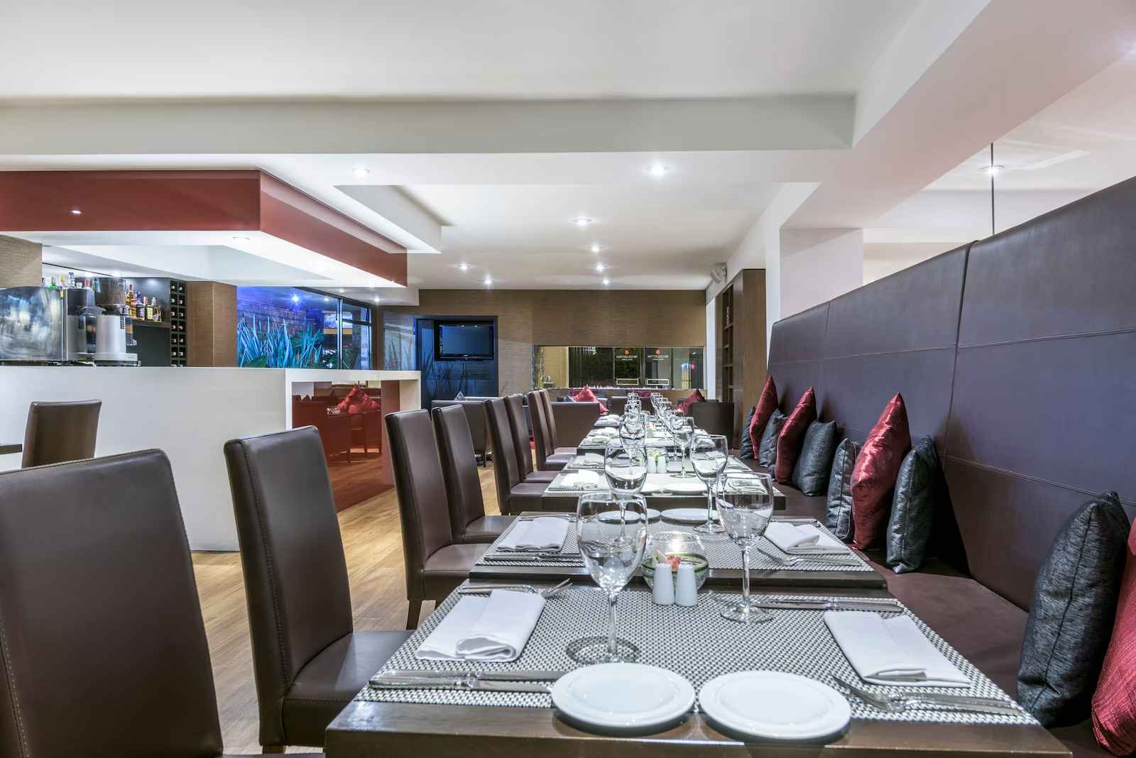  Salón de restaurante con sillas en cuero de color café. En las mesas hay varias copas de cristal y platos.