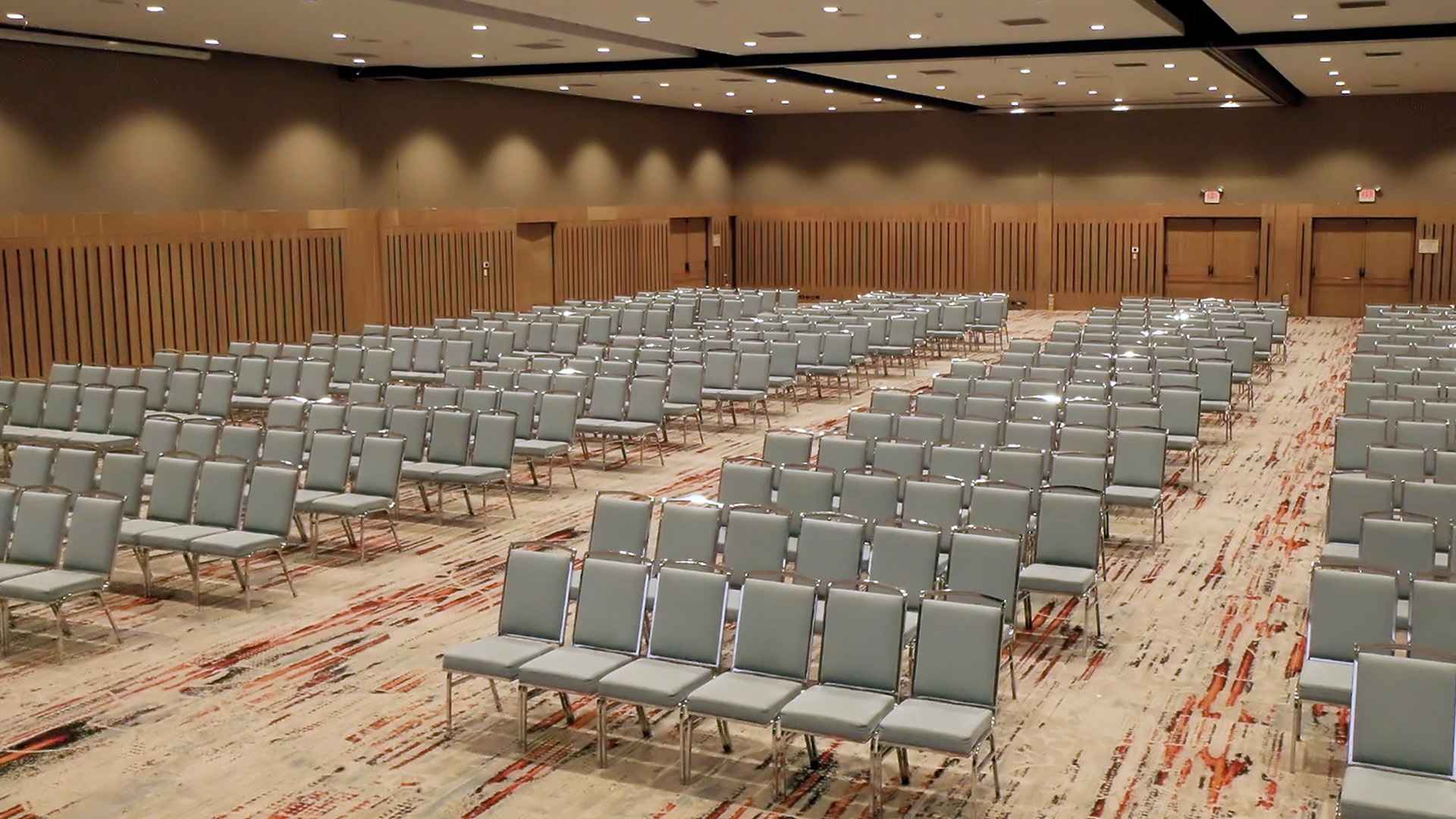  Gran salón decorado con madera con por lo menos un centenar de sillas grises.