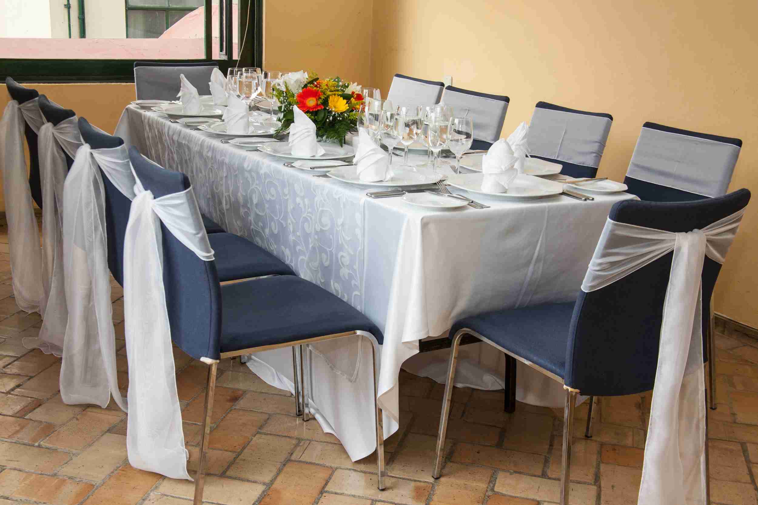 Primer plano de mesa rectangular vestida con mantel blanco. Hay varias copas, platos y cubiertos sobre la mesa.