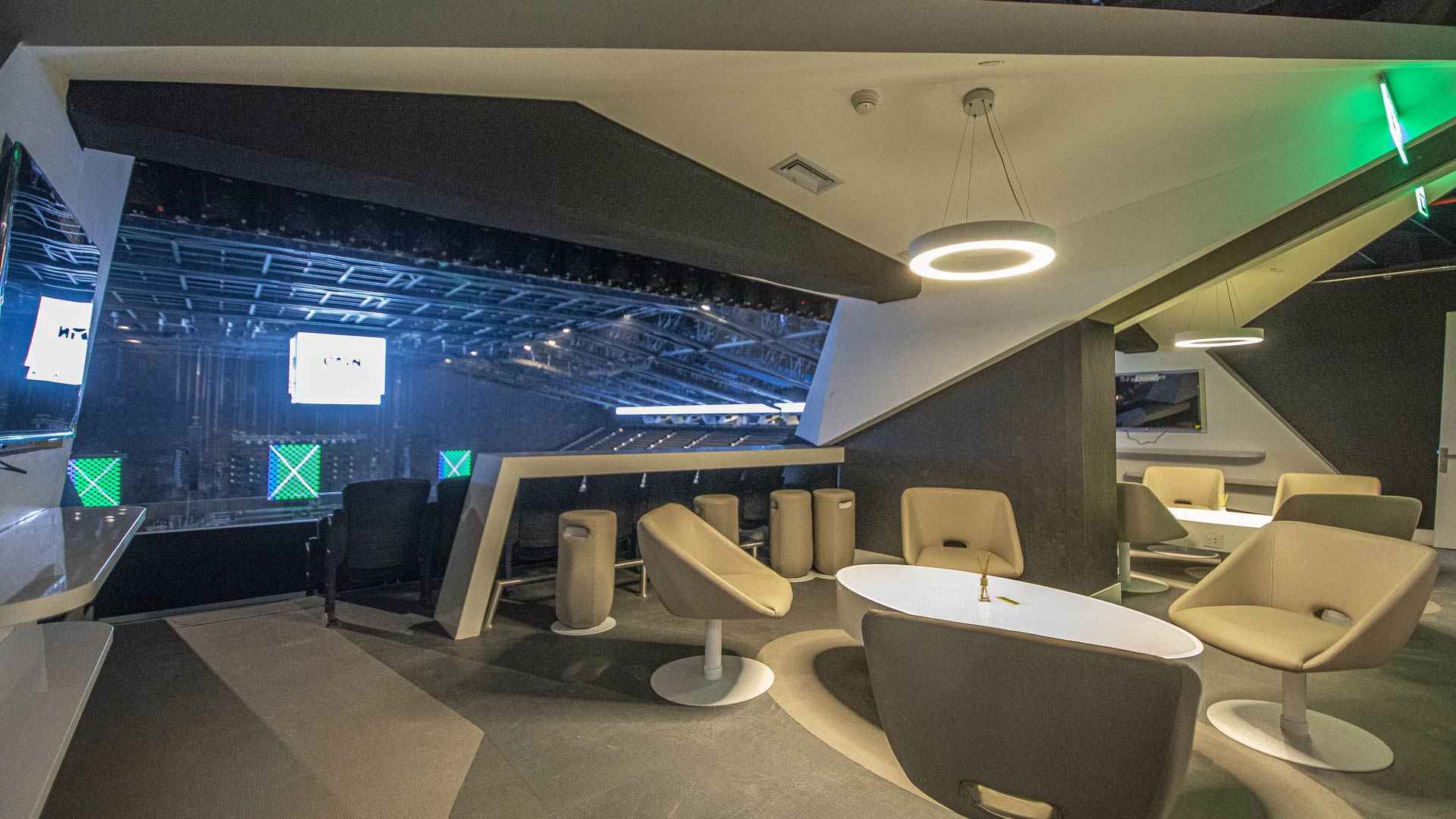 Concert venue private box. It has several chairs, a round table, and a bar with comfortable stools. The space is enclosed with glass overlooking the stage.