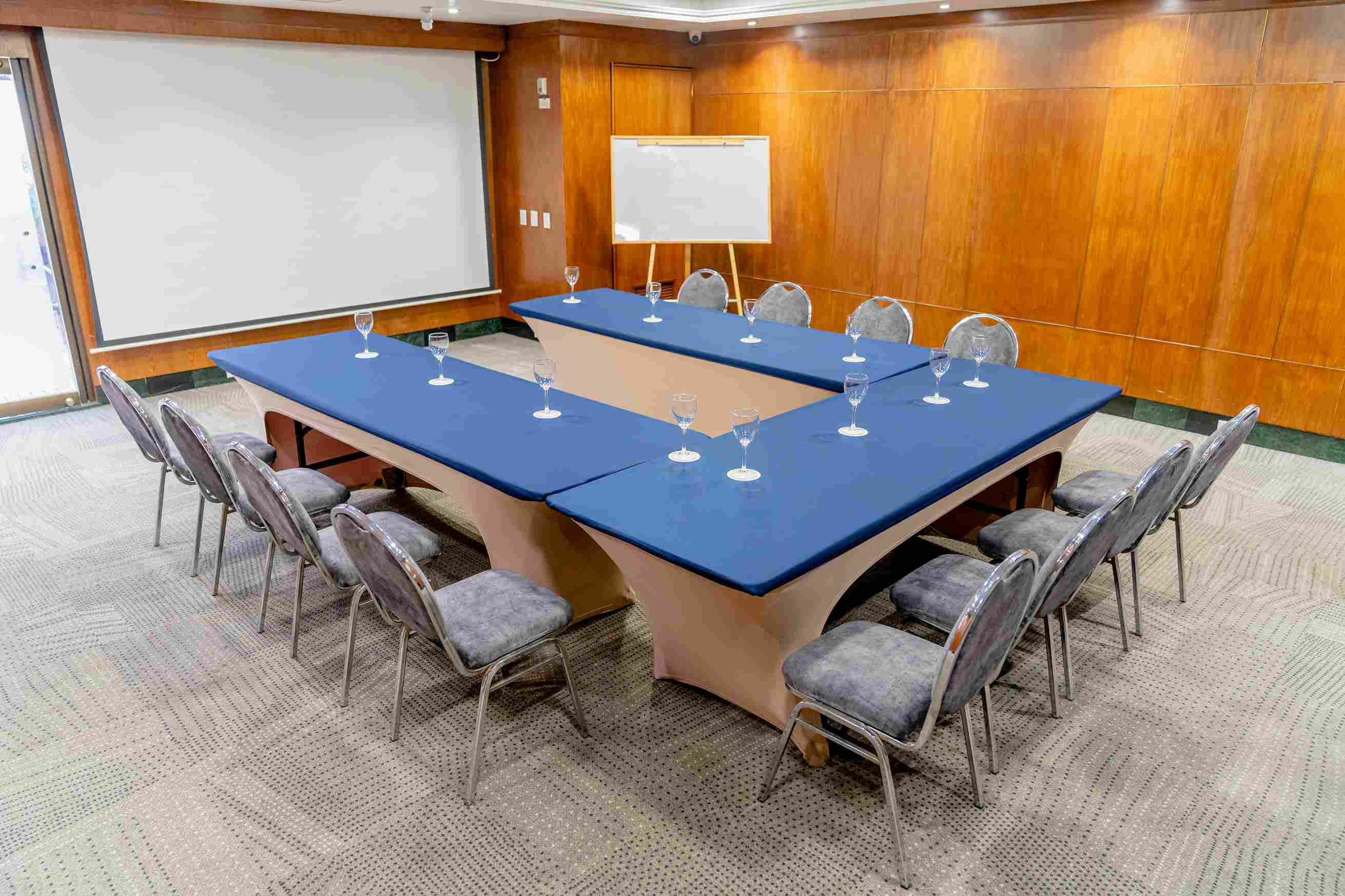 Salón con paredes de madera y una mesa en forma de U. Hay una pantalla de videobeam.