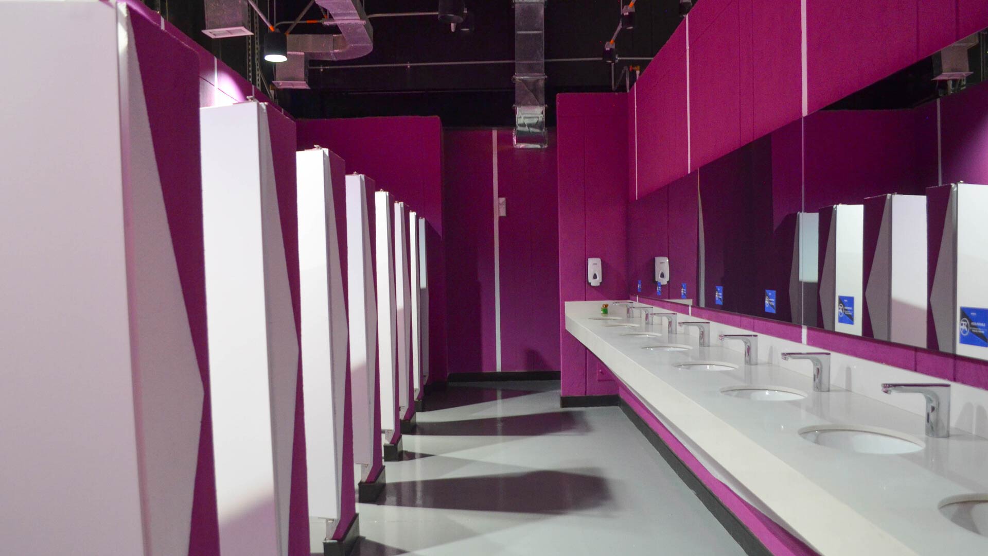 A modern restroom in pink and white tones, with several sinks and a rectangular mirror in front of them.