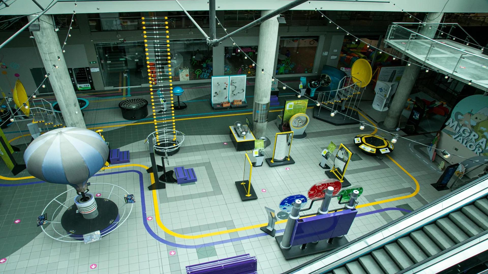 Interior space viewed from above, like a museum, where curious elements can be seen, including a balloon, a dinosaur skeleton, and a staircase leading up to the ceiling.