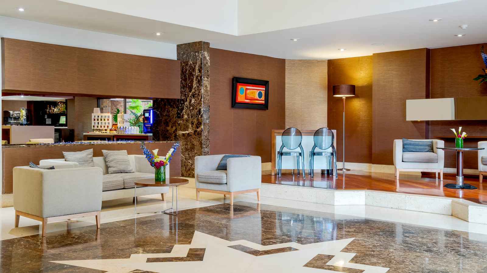 Pasillo central estilo recepción en la que hay un sofá y varias sillas amplias y abullonadas. El salón tiene un piso en cerámica café resplandeciente.