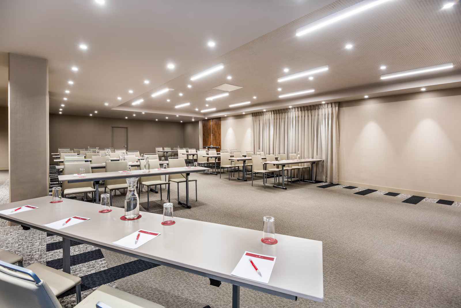 Salón amplio y entapetado dispuesto para conferencias con varias mesas y sillas alrededor.