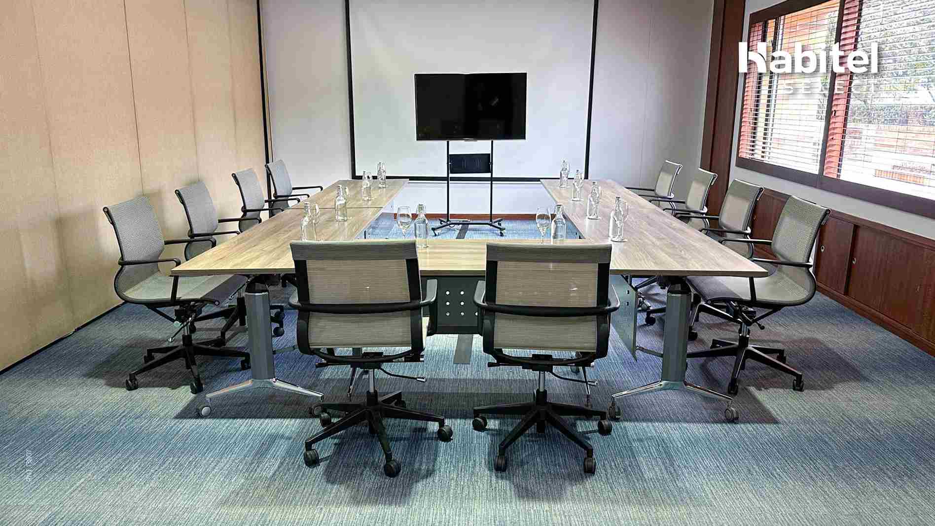  Salón pequeño con una mesa en forma de U. Hay varias sillas alrededor, un televisor y una pantalla de videobeam.