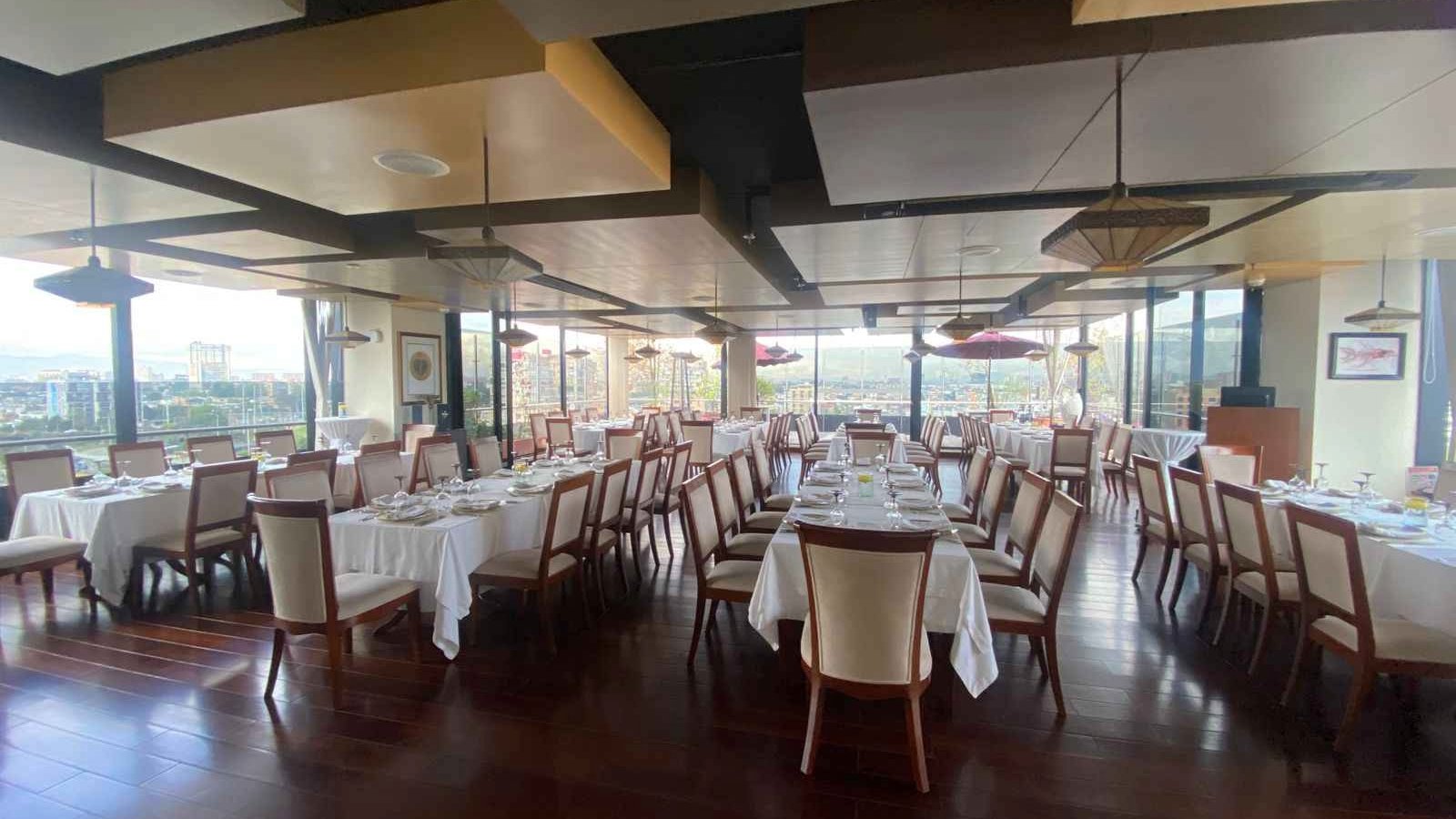  Un gran salón con 4 filas de mesas con orientación vertical. Hay grandes ventanales alrededor de las mesas.