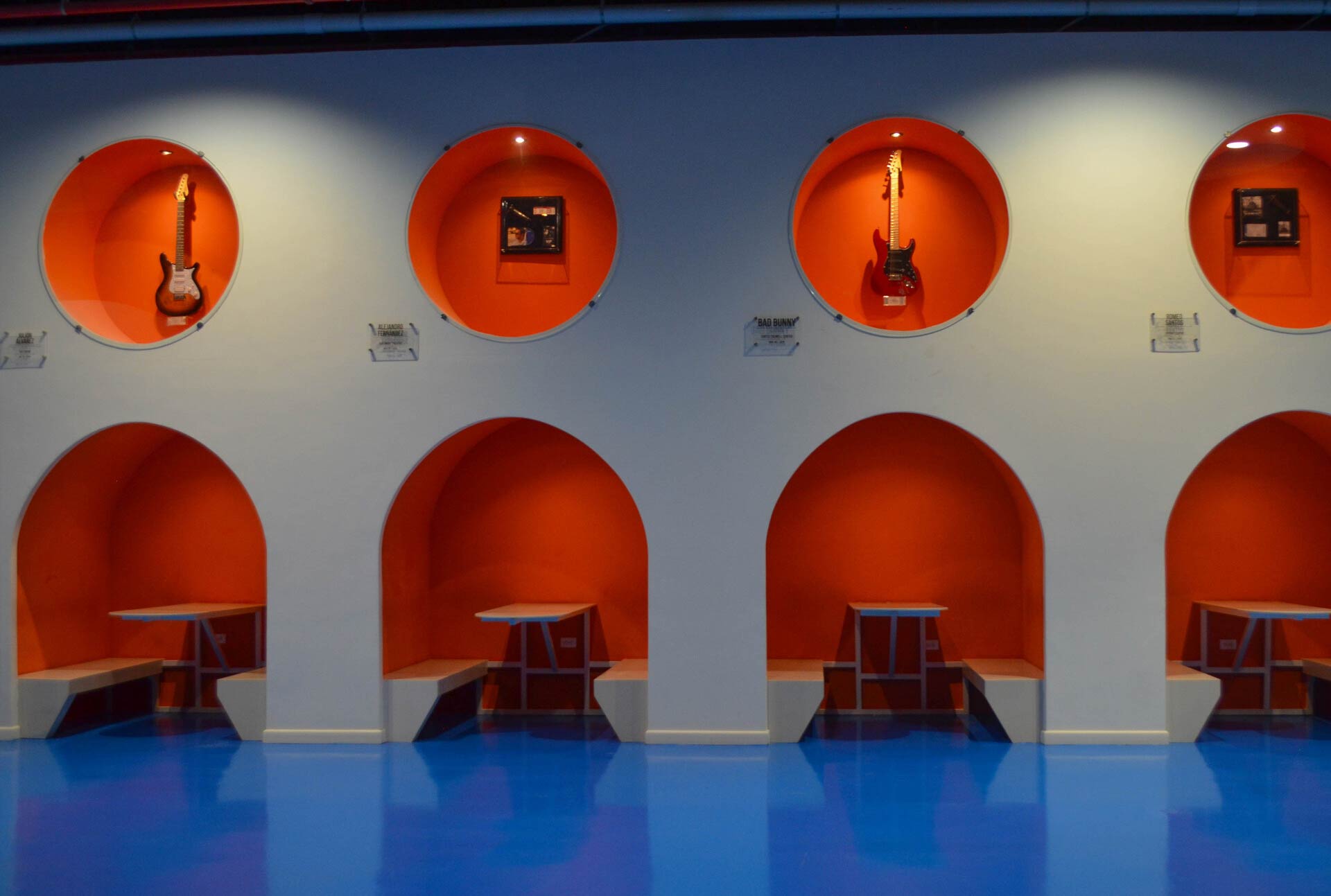 Lounge featuring four small galleries, each with a table and chair. Above each station, an inset wall niche displays an electric guitar.