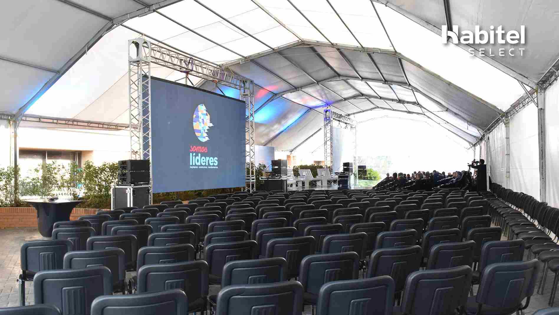 Salón de reuniones cubierto con una lona blanca, por lo menos un centenar de sillas y una pantalla gigante de videobeam.