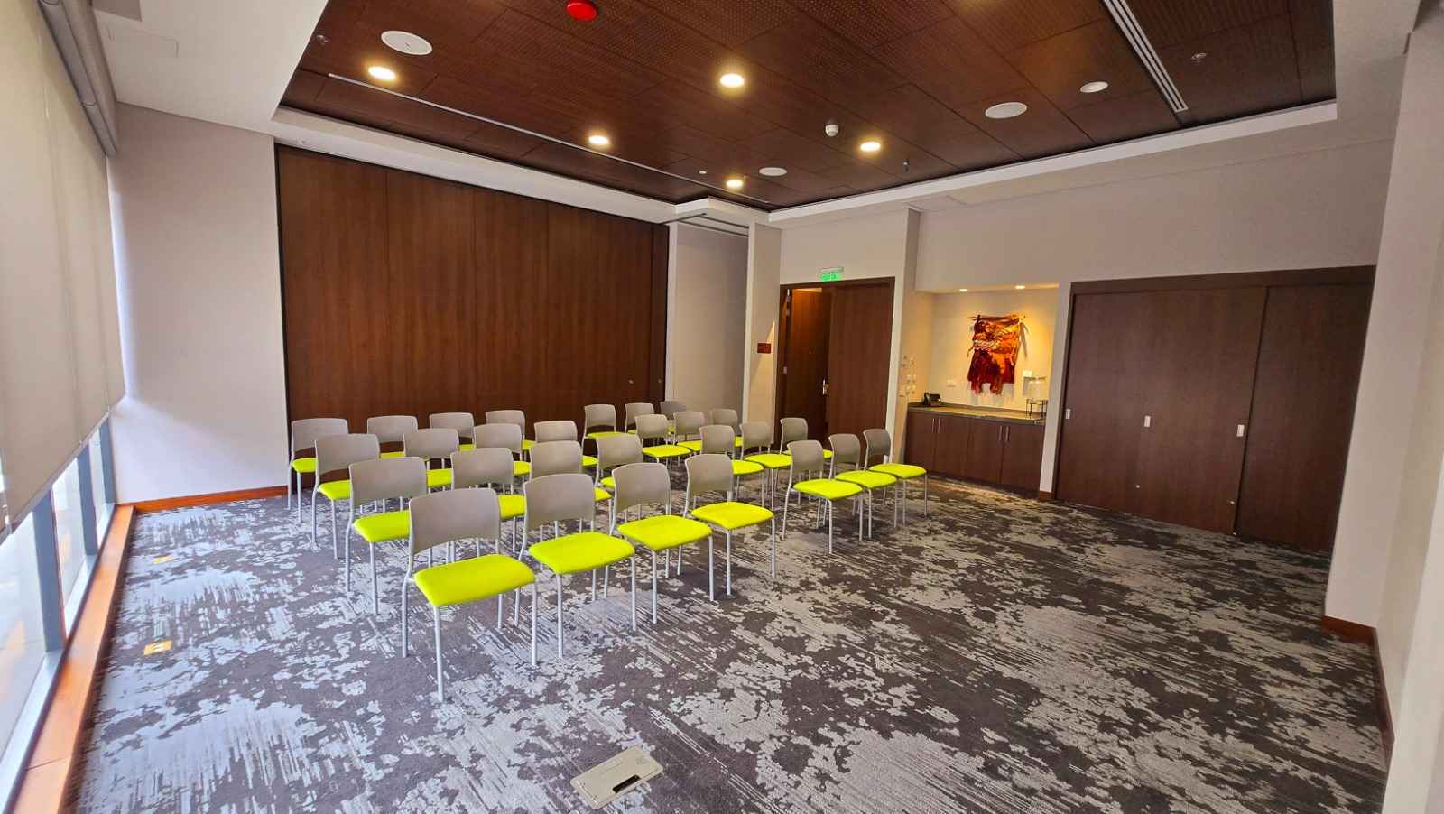 Salón mediano con más de treinta sillas de color amarillo y blanco. Hay una mesa dispuesta para cafetería.
