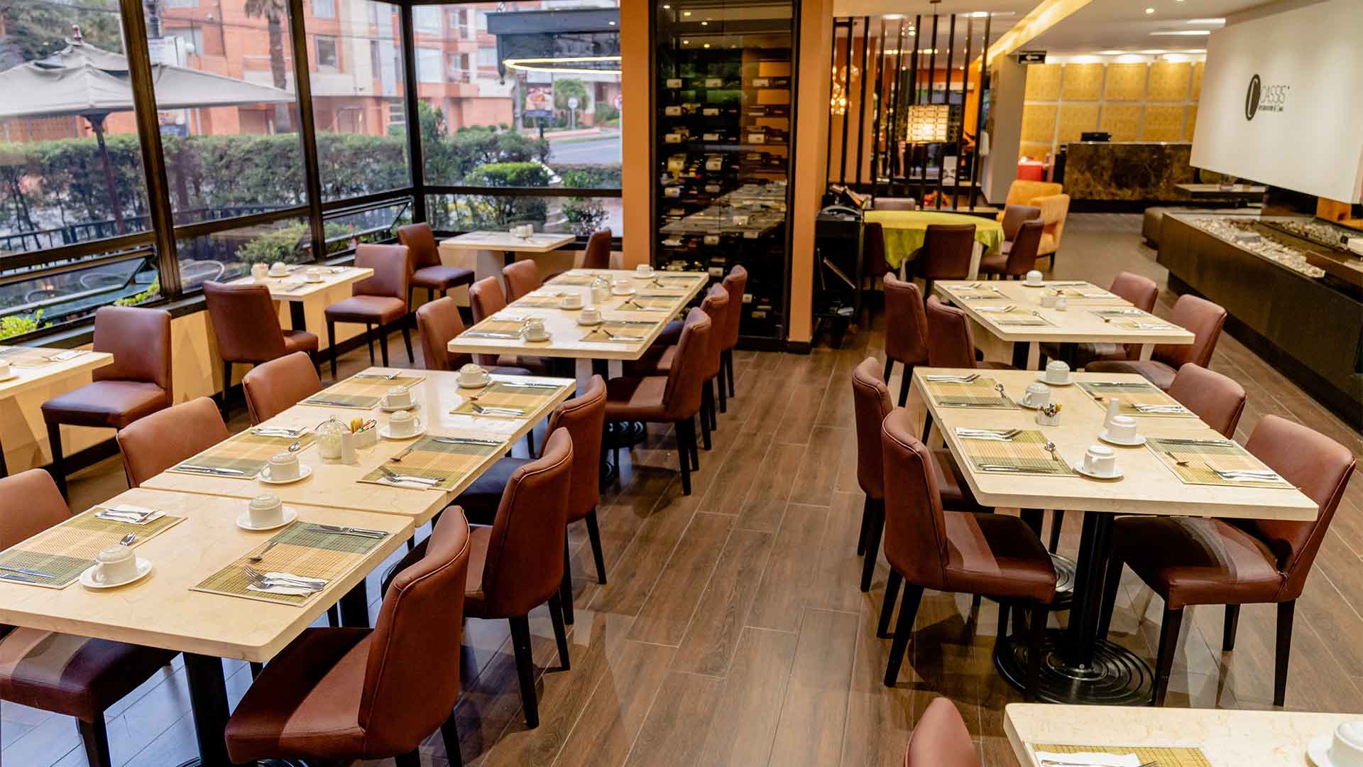  Salón comedor con varias mesas rodeadas de 6 sillas cada una. Al fondo hay una cava de vinos, una gran chimenea rectangular y al frente un ventanal hacia la calle.