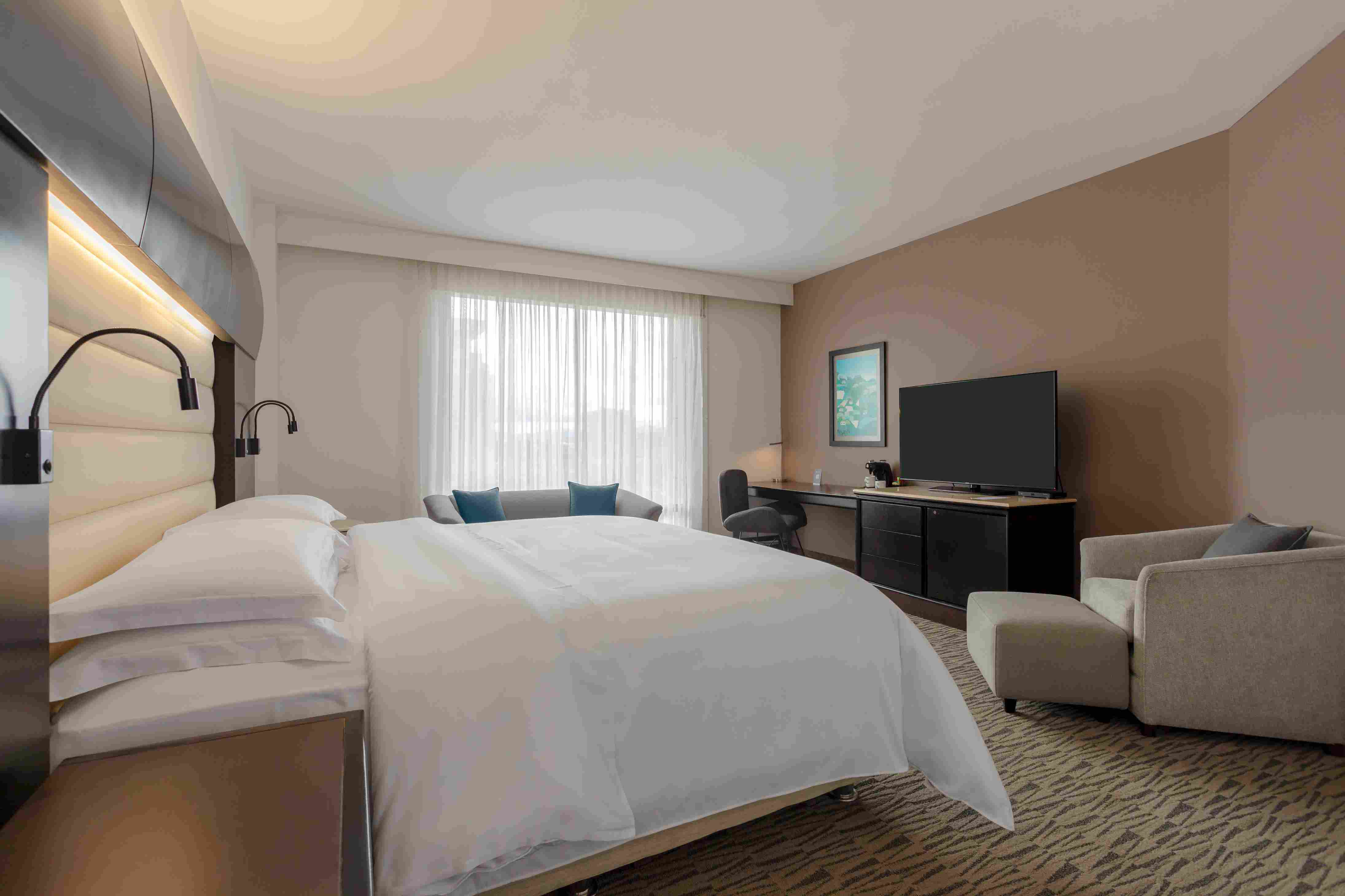 Amplia habitación con una cama con tendido blanco, una mesa con un televisor y un sofácama.