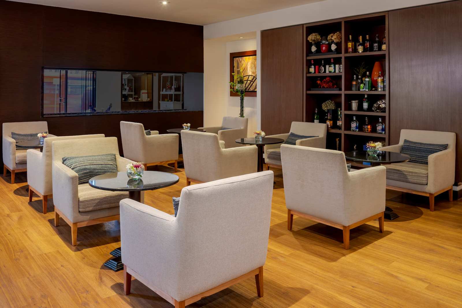 Salón estrecho con varias mesas redondas y sillas amplias y abullonadas. A un lado en una pared hay un escaparate con botellas de licor.