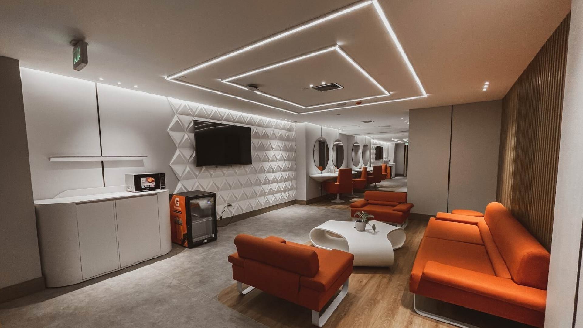 Dressing room-style lounge equipped with sofas, a table, a refrigerator, and several mirrors.