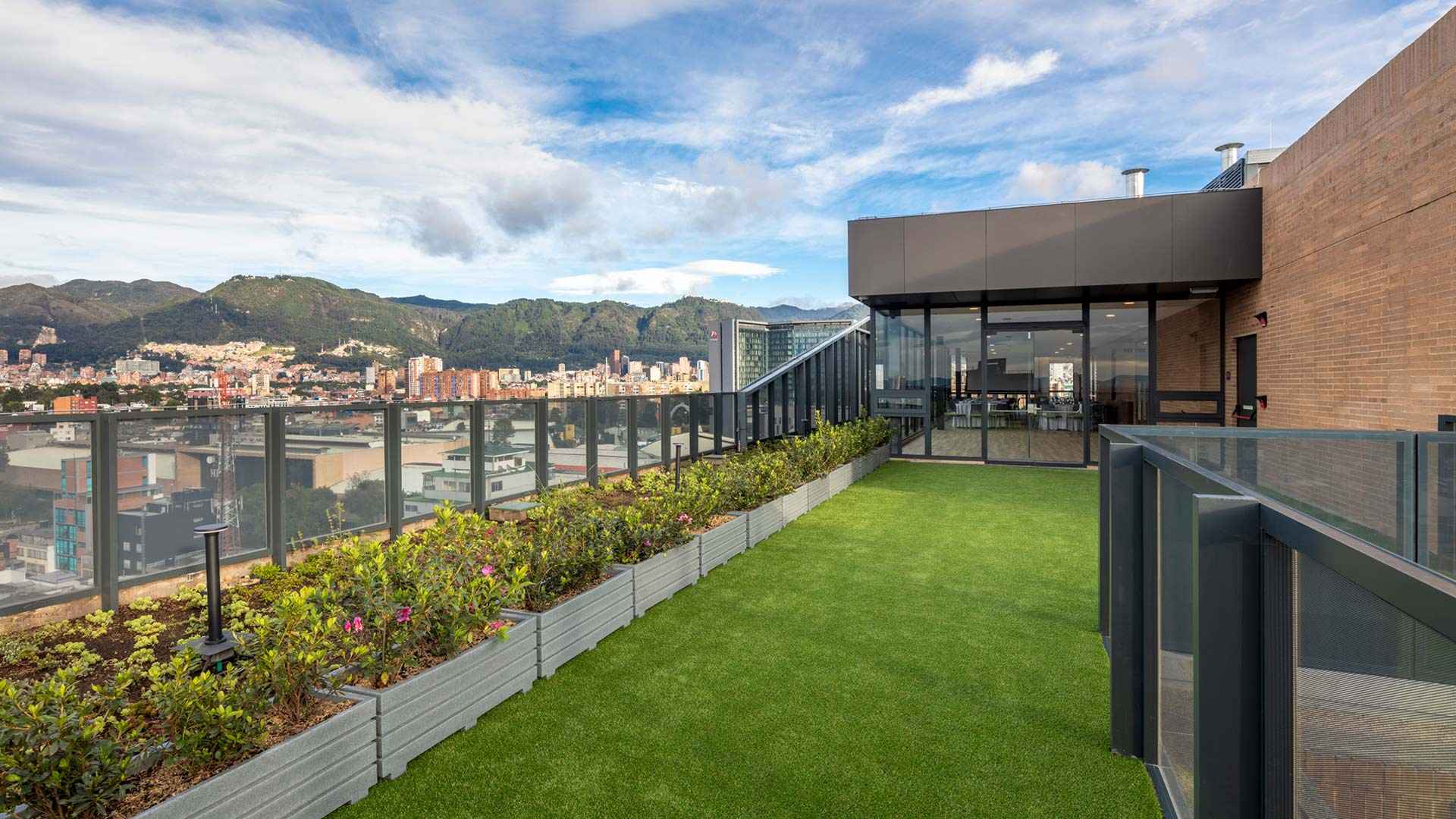  Terraza con cesped artificial desde donde se ve el oriente de Bogotá y sus cerros. El cielo está azul con algunas nubes.