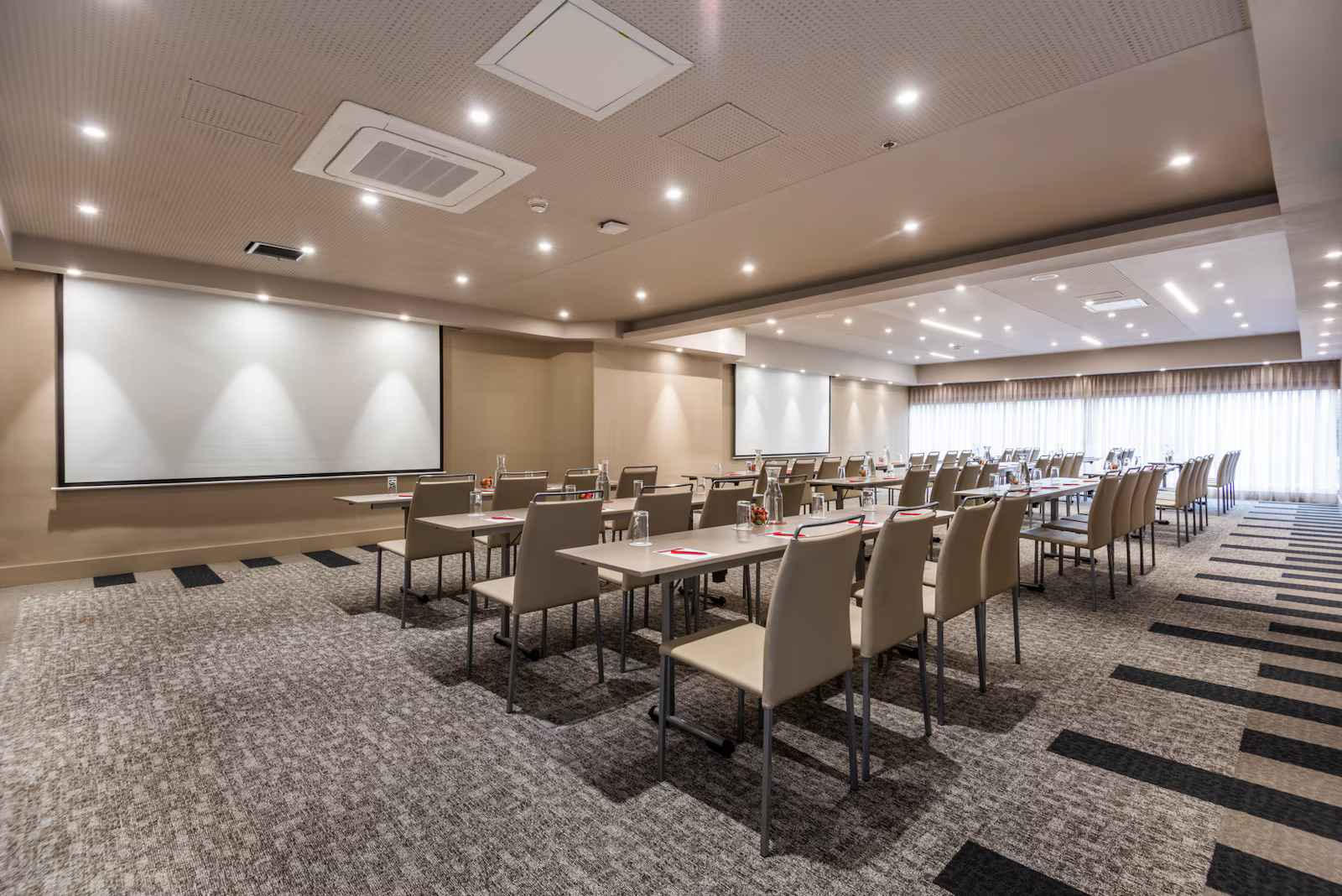 Salón amplio y entapetado dispuesto para conferencias con varias sillas organizadas de manera horizontal y mirando hacia una pantalla de proyector al frente.