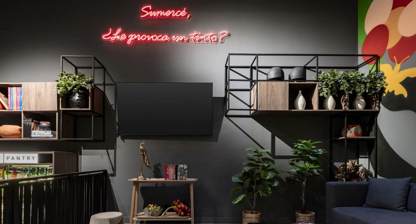 Salón en el que destacan dos escaparates en  una pared, repletos de libros y plantas. También hay un televisor y un sofá azul.