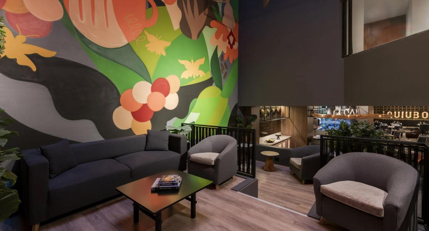 Salón de tres plantas de madera en el que destacan en la tercera un sofá y dos poltronas. También hay una pequeña mesa cuadrada en el centro. En la segunda una mesita redonda y una silla, y en la primera varias plantas.