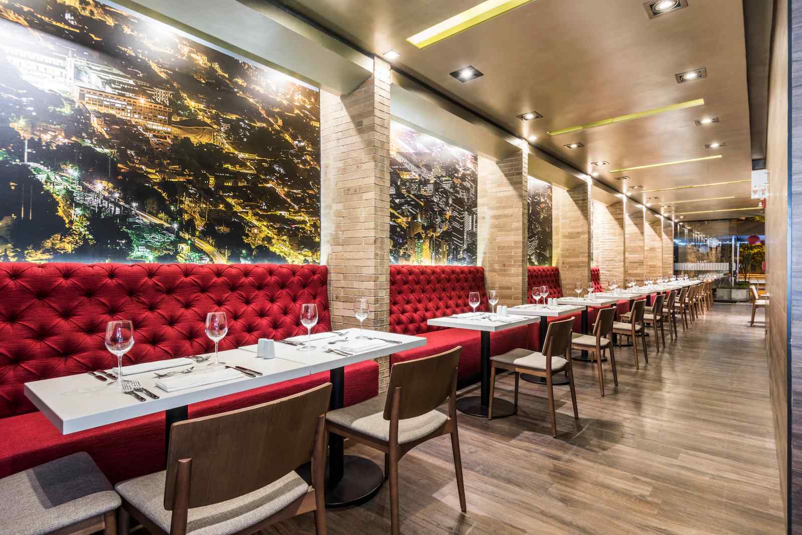  Salón rectangular, como un comedor, con varios sofás en cuero de color rojo. Hay varias mesas con copas de cristal. Al fondo hay un tapiz de una panorámica de una ciudad de noche.