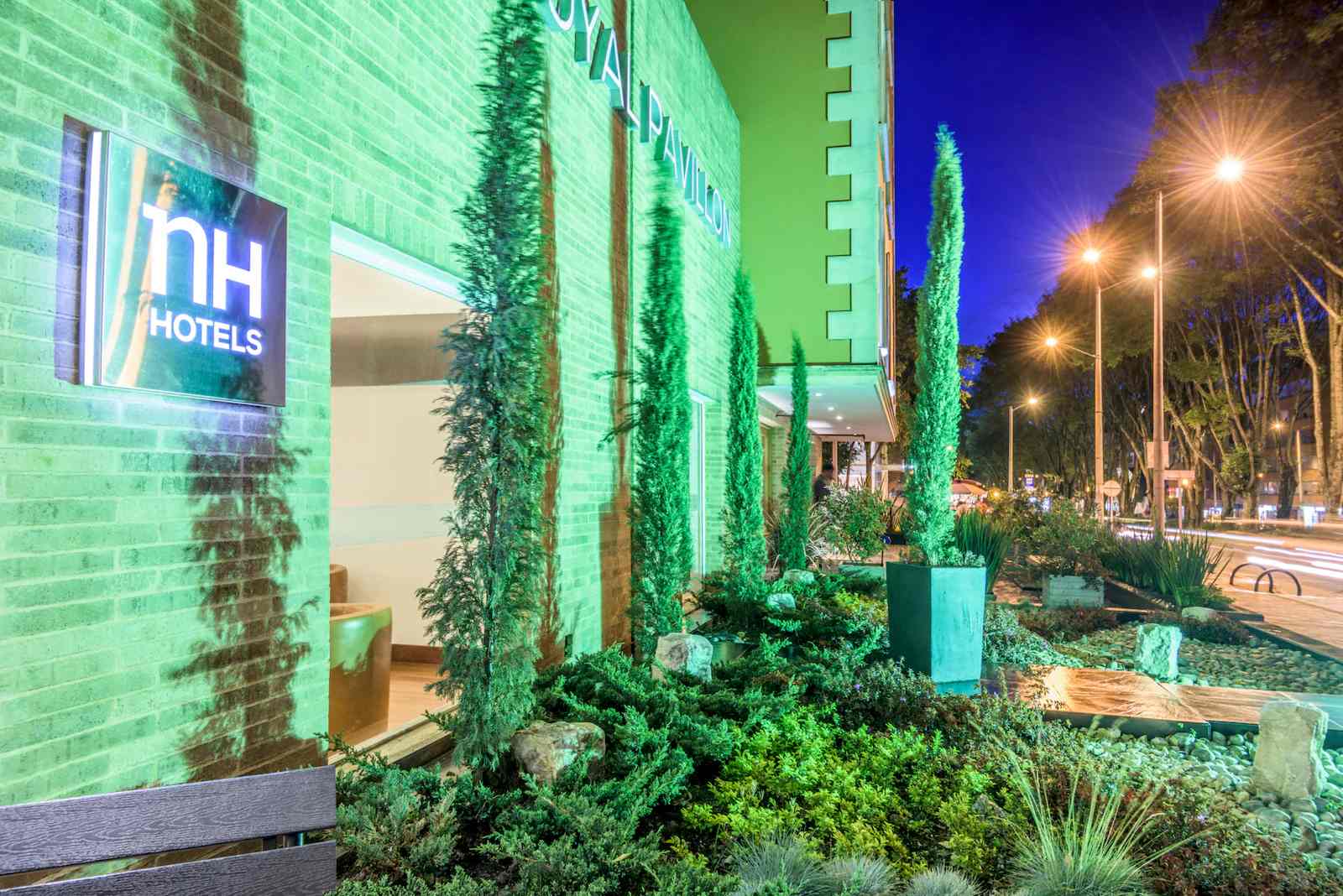  Exterior de edificación de una sola planta, en el que resalta una gran ventana rodeada de pinos y otra vegetación.