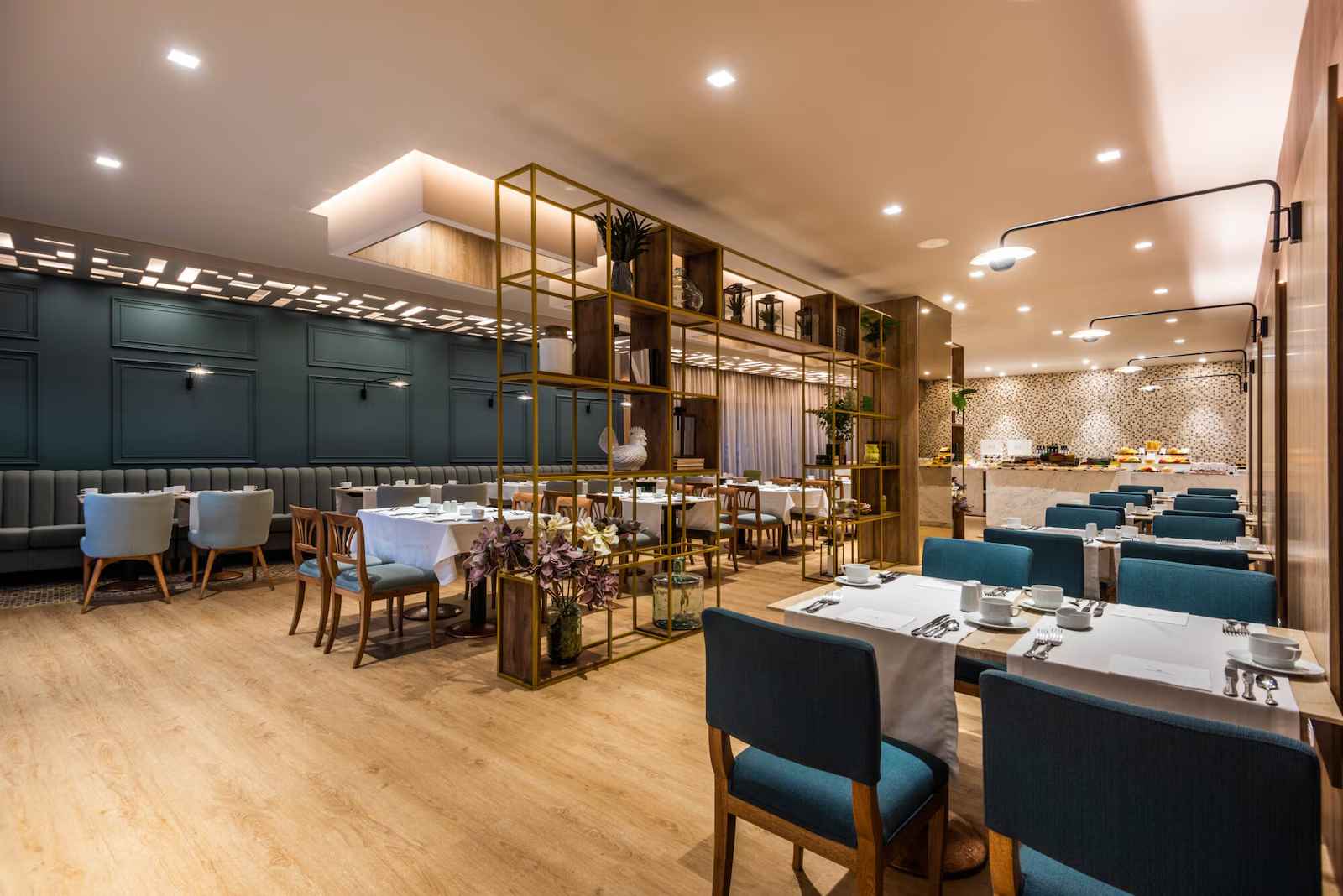 Comedor pequeño con varias mesas de cuatro puestos. El salón está dividido por una estructura de madera estilo estante en donde reposan varias plantas.