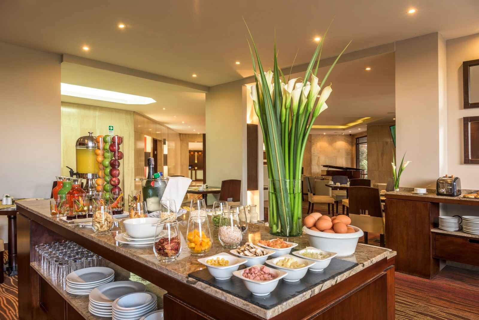 Salón en el que hay una mesa amplia sobre la que hay huevos, trozos frutas y de cereales. La mesa está decorada con un arreglo floral.