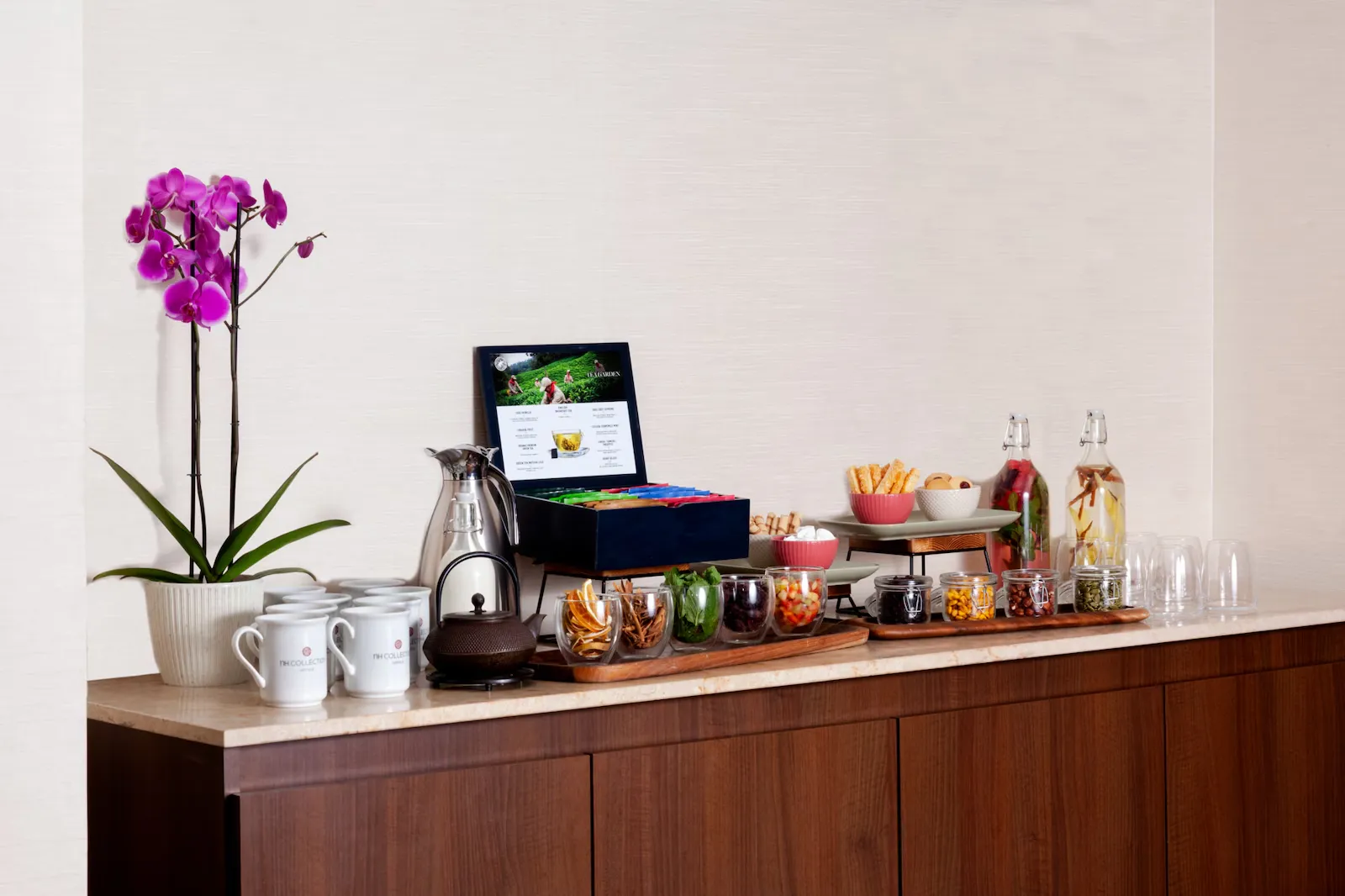 Mesa en una pared repleta de pocillos e infusiones de té. Se destaca una matera con una orquídea.