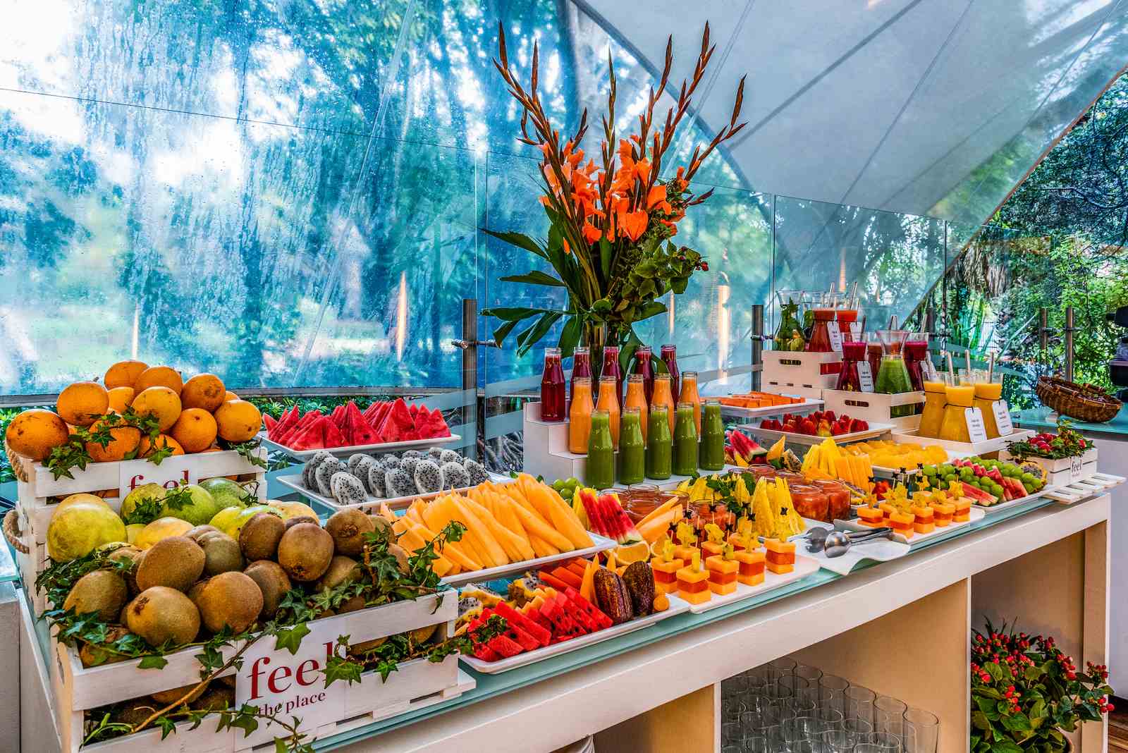  Pequeño salón con una repisa repleta de trozos de fruta, botellas de jugo y un gran arreglo floral.