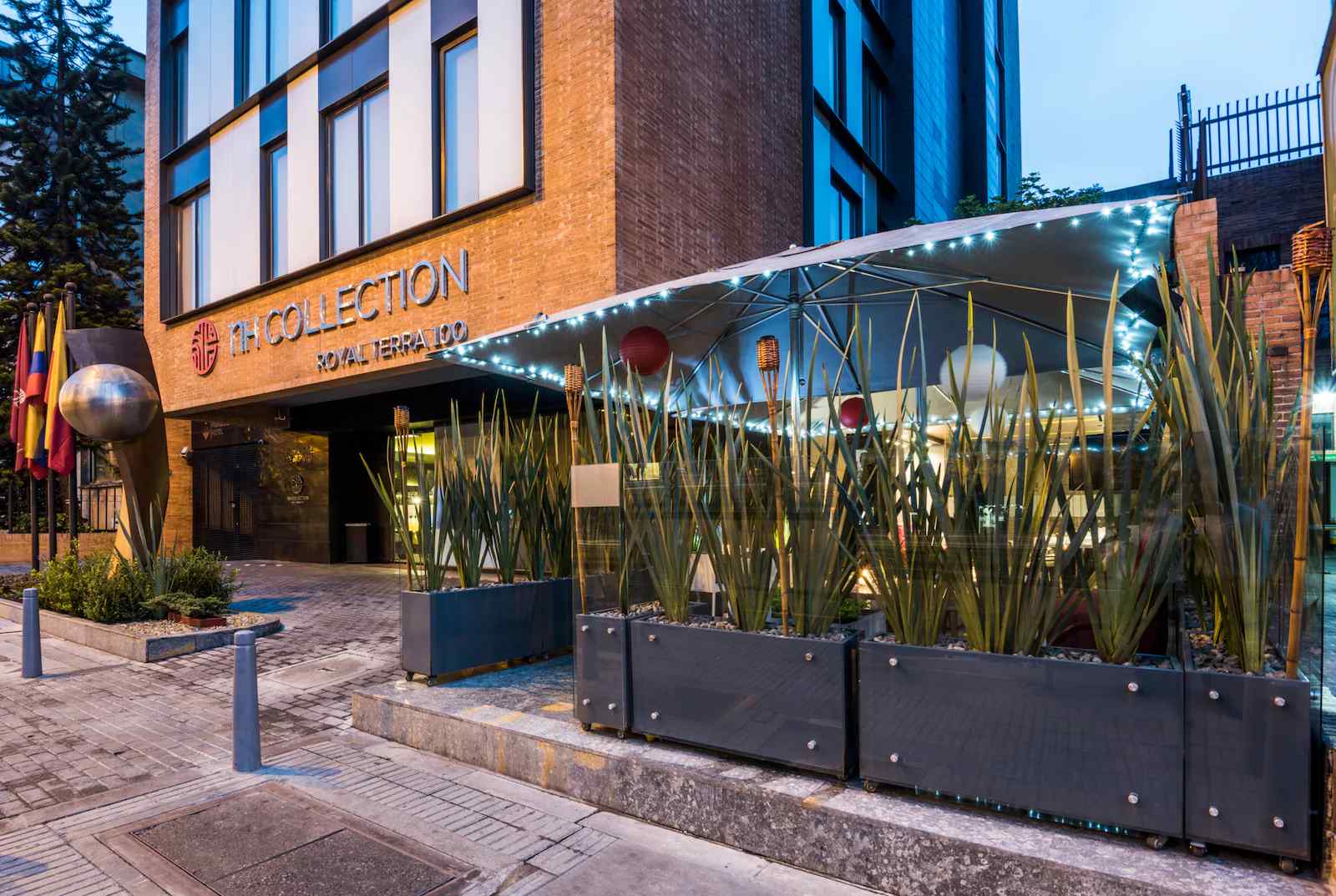  Fachada de edificación en la que sobresale una especie de terraza iluminada con luz artificial. En la entrada hay un aviso con una leyenda que dice: "nH Collection".