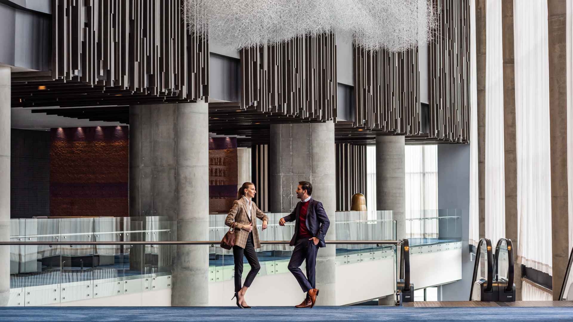 Un hombre y una mujer joven en un edificio, se ven conversando de forma tranquila, donde destacan tres columnas de concreto. 