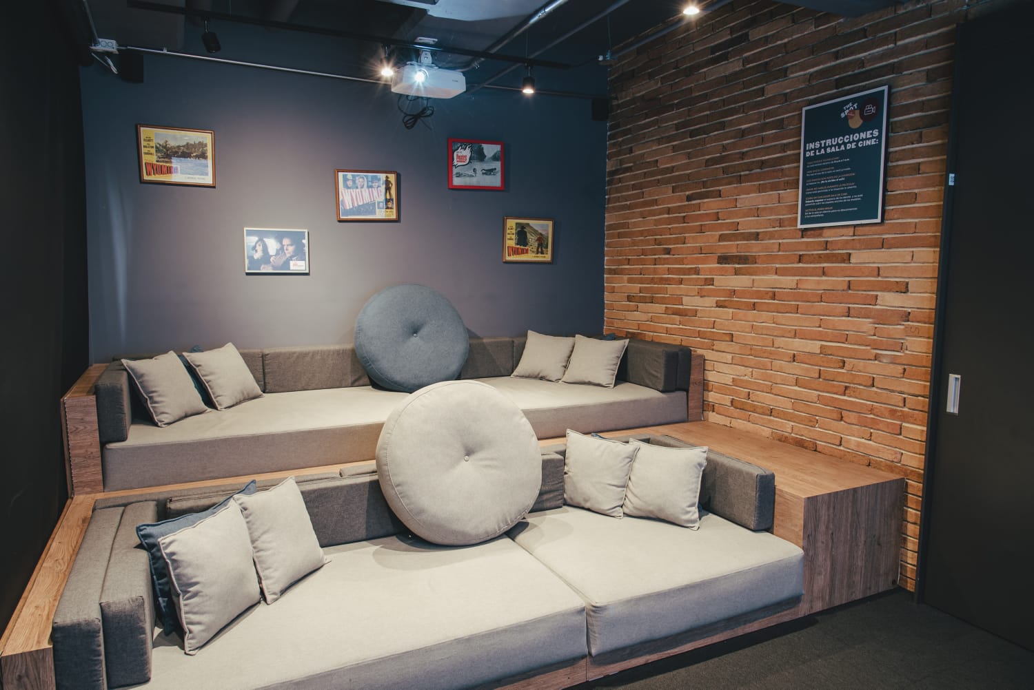 Salón pequeño cuadrado con dos poltronas muy grandes, y en el techo un reproductor de videobeam.