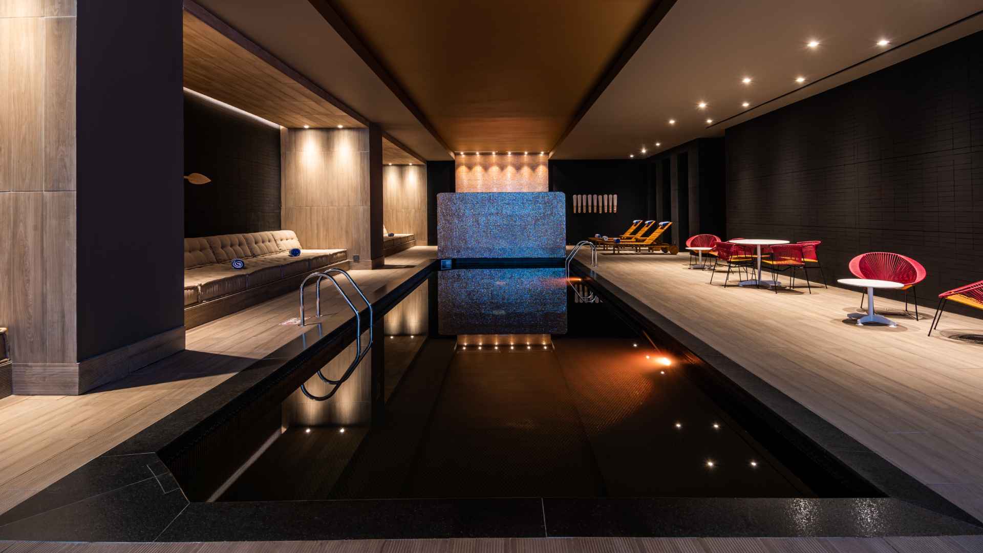 Salón donde hay una piscina rodeada por sillas, algunas de ellas reclinables.
