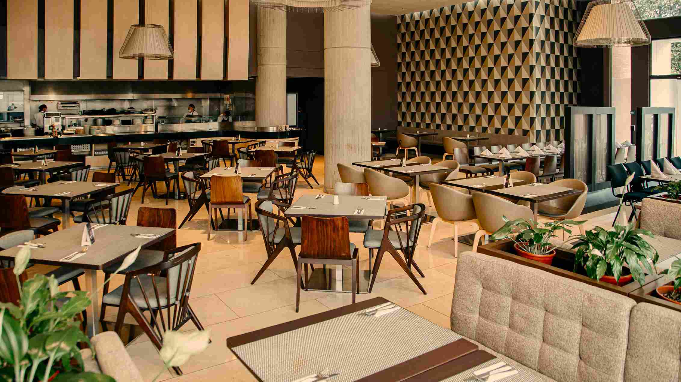  Diner-style room featuring several tables surrounded by chairs. In the background, two people can be seen at a food delivery counter.