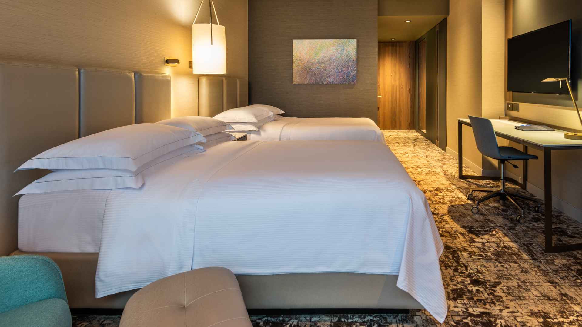 Habitación entapetada en la que se ven dos camas amplias, una mesa y un televisor.
