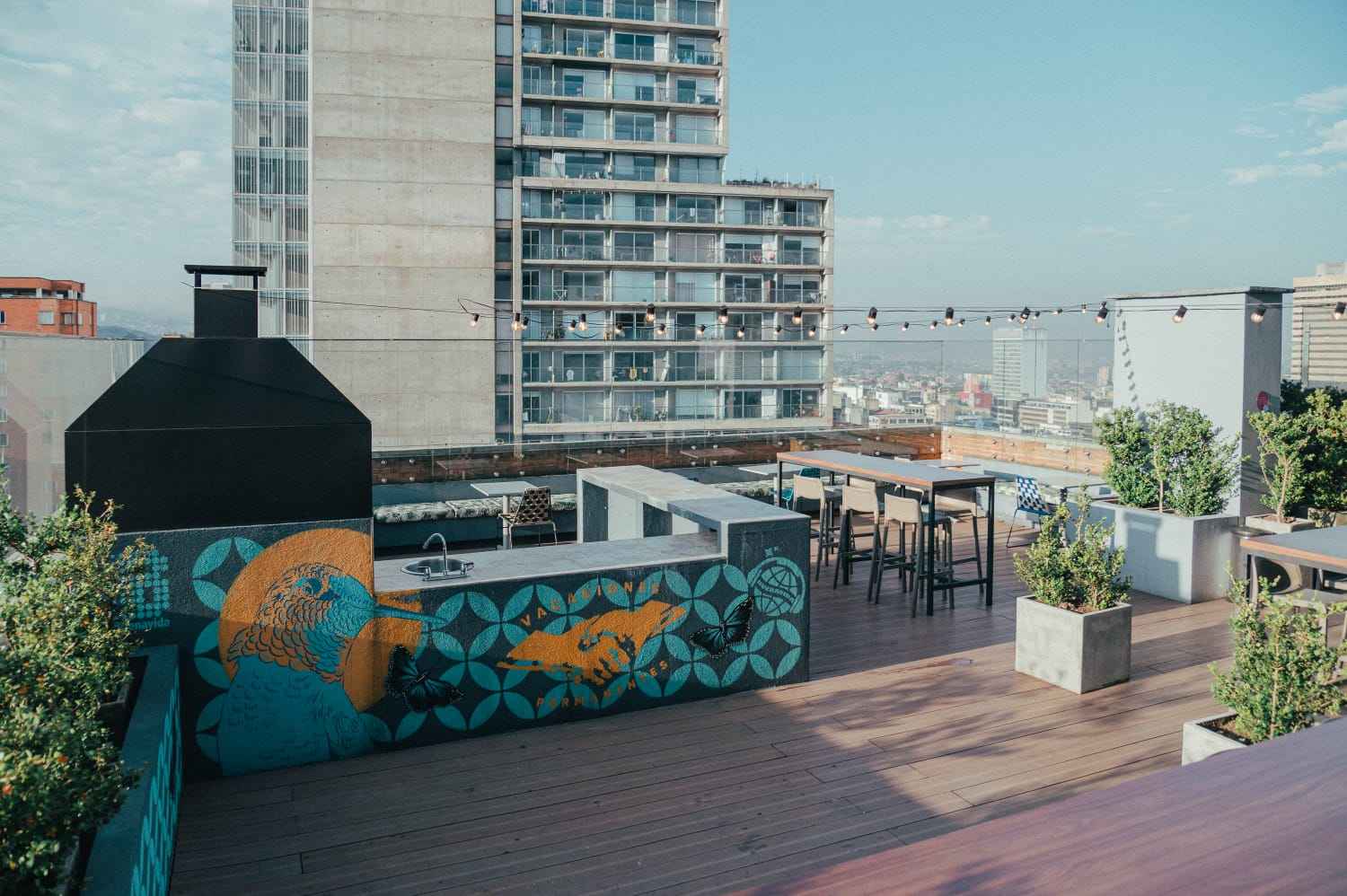  Terraza en piso alto, descubierta, con una larga mesa rodeada de sillas, y desde la que se observan edificios cerca y lejos.