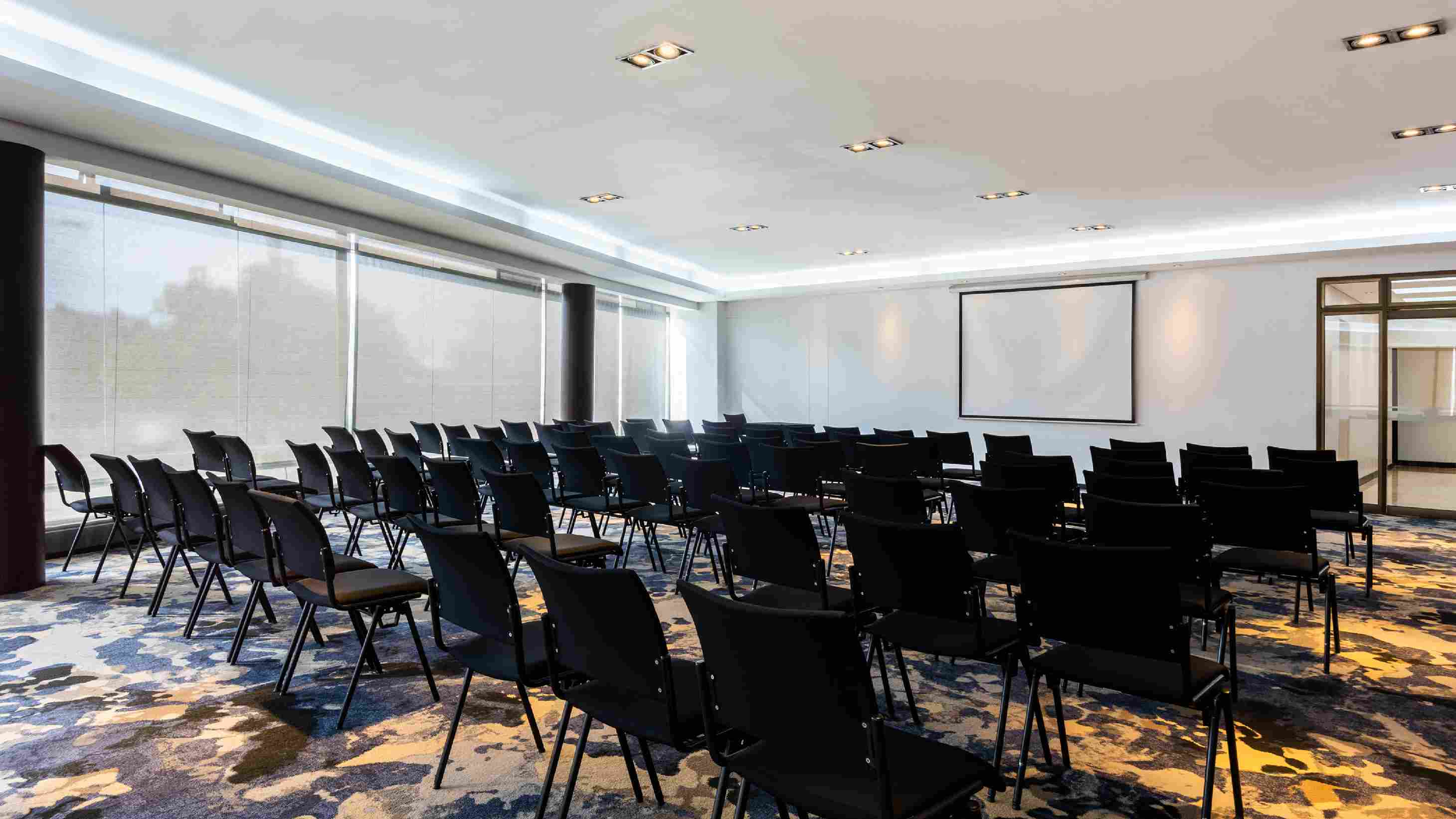 Gran salón con por lo menos cincuenta sillas, todas de frente a una pantalla de videobeam. A un lado hay un gran ventanal cubierto por cortinas blancas.