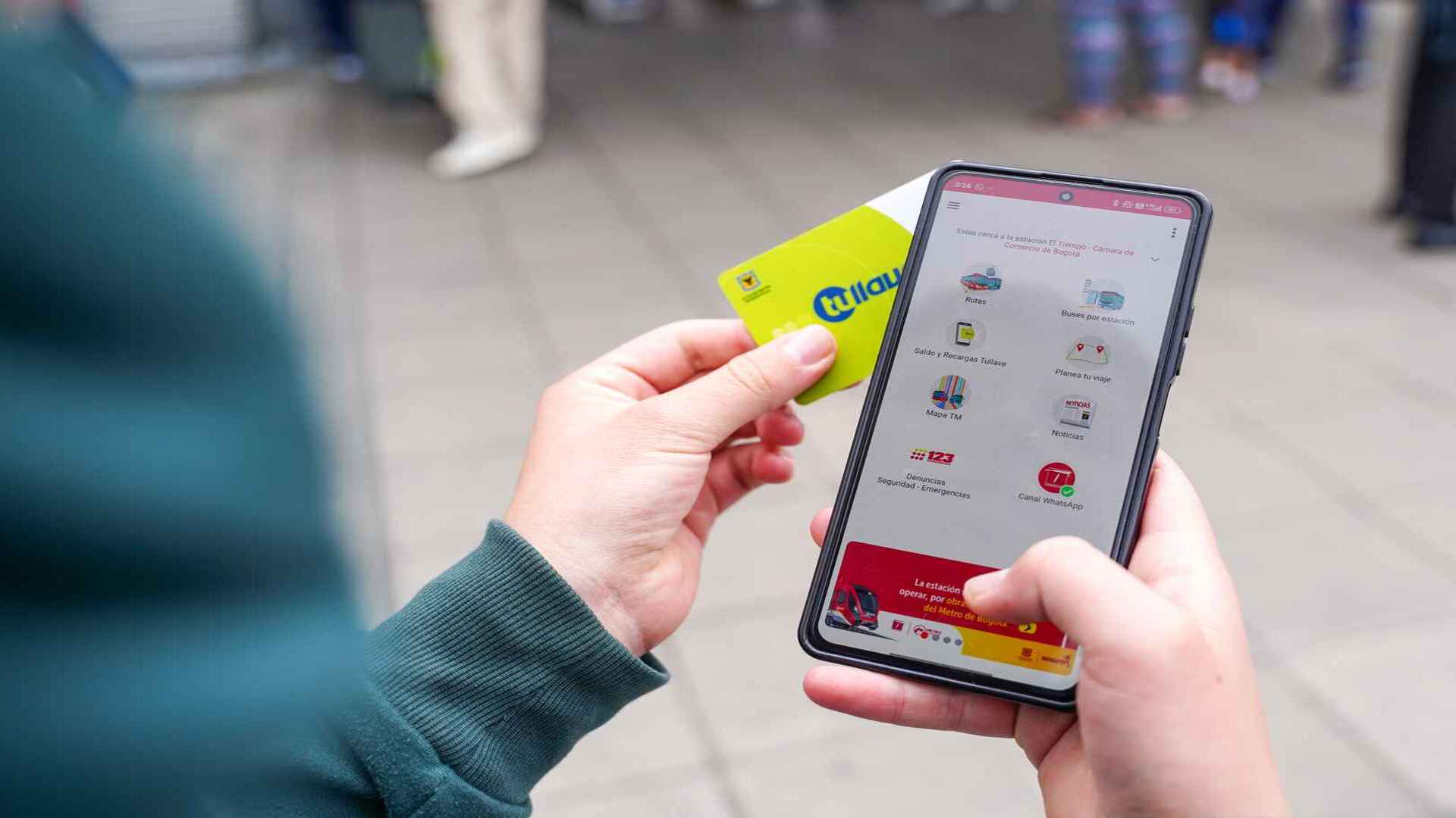 Manos sosteniendo una tarjeta de transporte y un smartphone con una aplicación de movilidad en Bogotá.