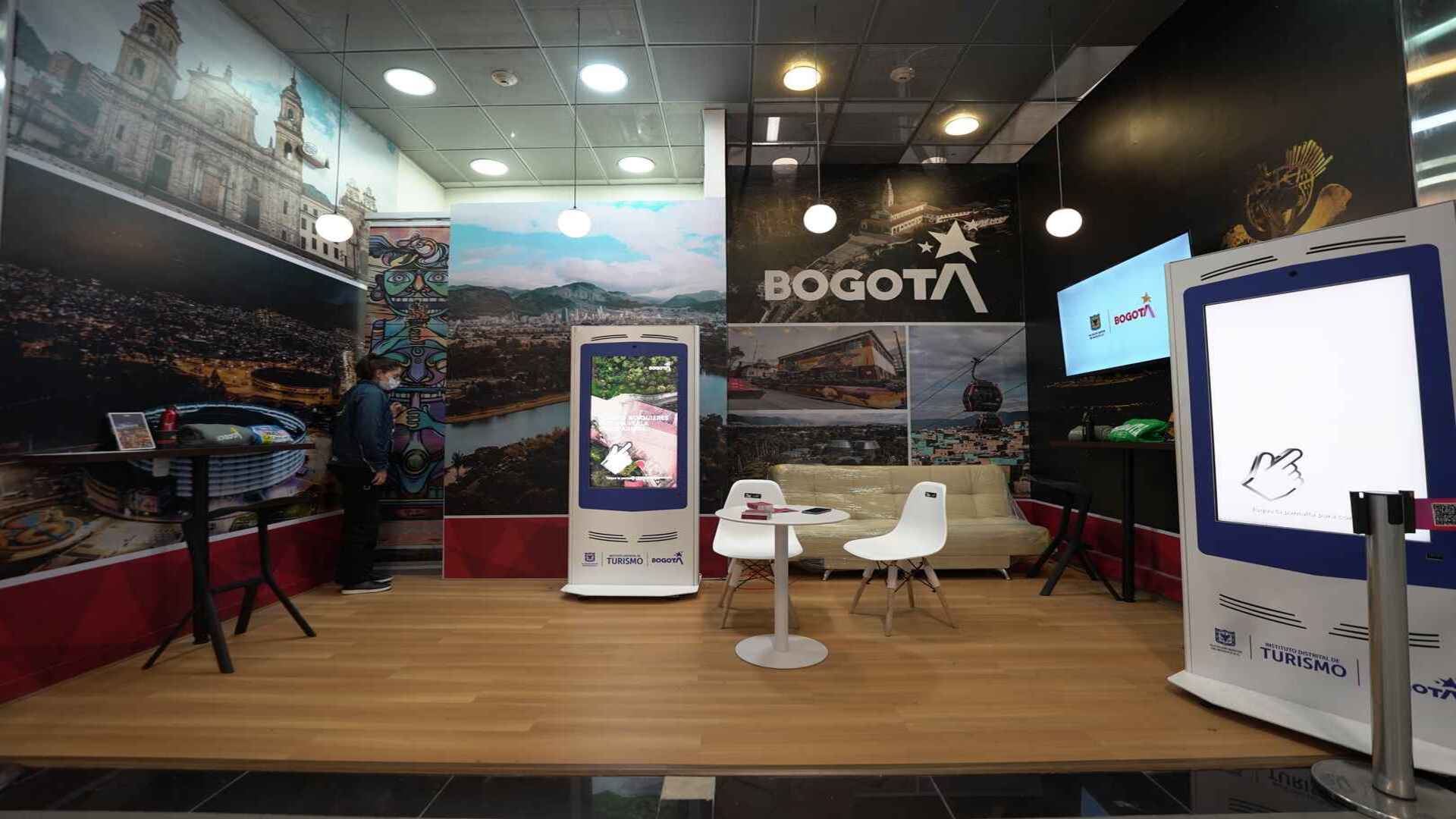 Un moderno stand de información turística de Bogotá con pantallas digitales y vibrantes imágenes de la ciudad.